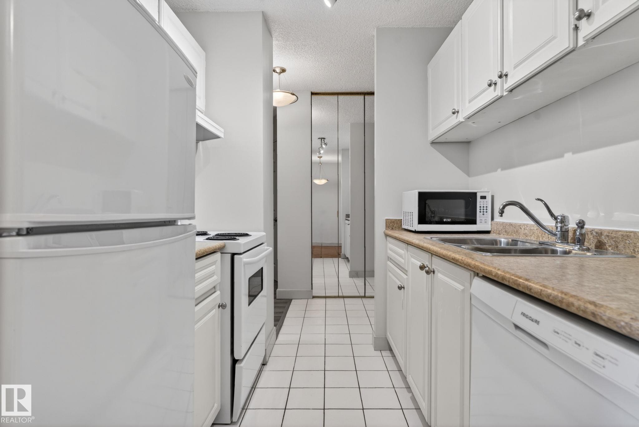 Galley kitchen featuring white cabinetry, white appliances, and a light-colored countertop - #412 13910 Stony Plain Rd Nw, Edmonton, AB - Indoor Photo Showing Kitchen With Double Sink