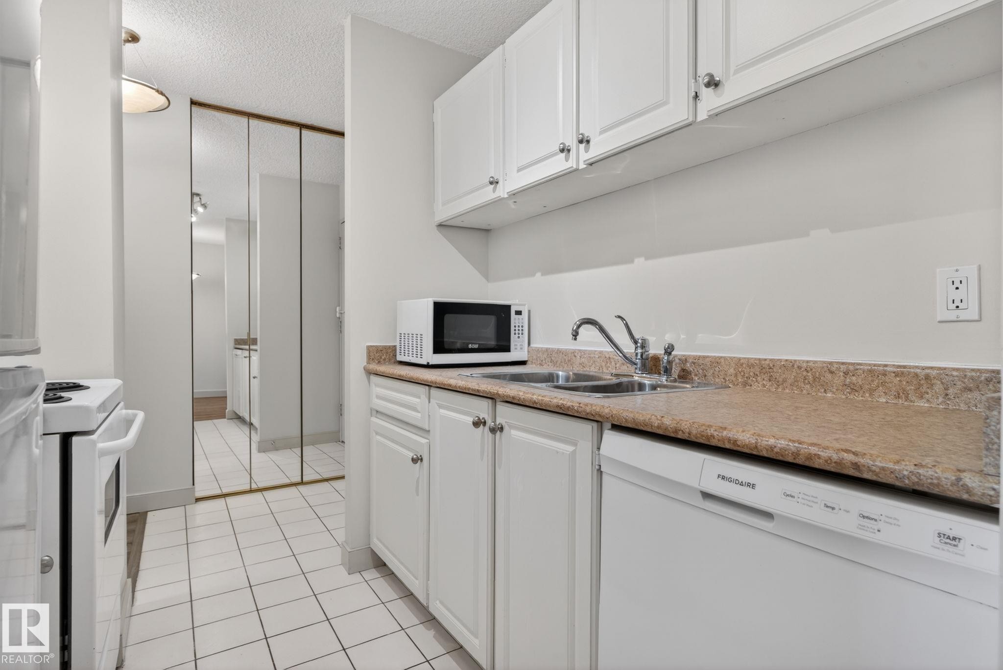 Galley kitchen featuring white cabinetry, a built-in dishwasher, and a double basin sink - #412 13910 Stony Plain Rd Nw, Edmonton, AB - Indoor Photo Showing Kitchen With Double Sink