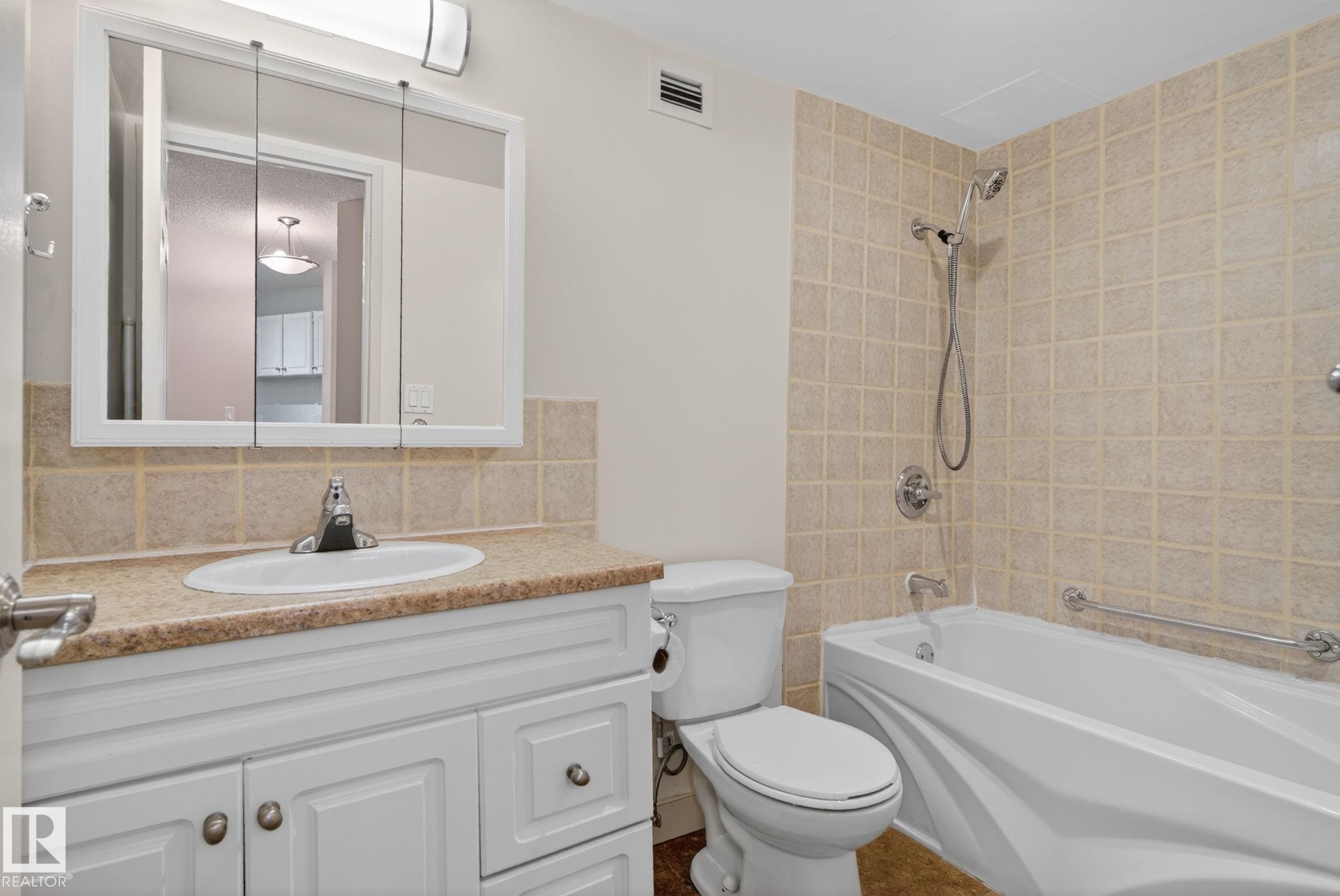 Bathroom featuring a white vanity with a light-colored countertop, an integrated sink, and a mirrored medicine cabinet - #412 13910 Stony Plain Rd Nw, Edmonton, AB - Indoor Photo Showing Bathroom