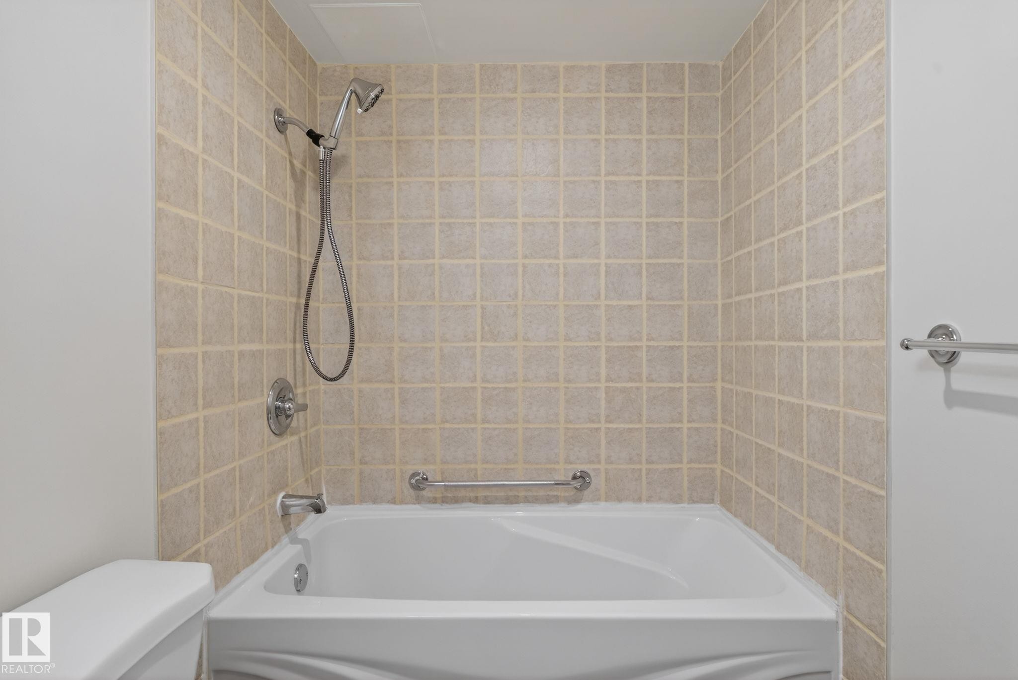 Bathroom tub and shower combination featuring neutral square wall tiles, chrome fixtures, and a white porcelain tub - #412 13910 Stony Plain Rd Nw, Edmonton, AB - Indoor Photo Showing Bathroom
