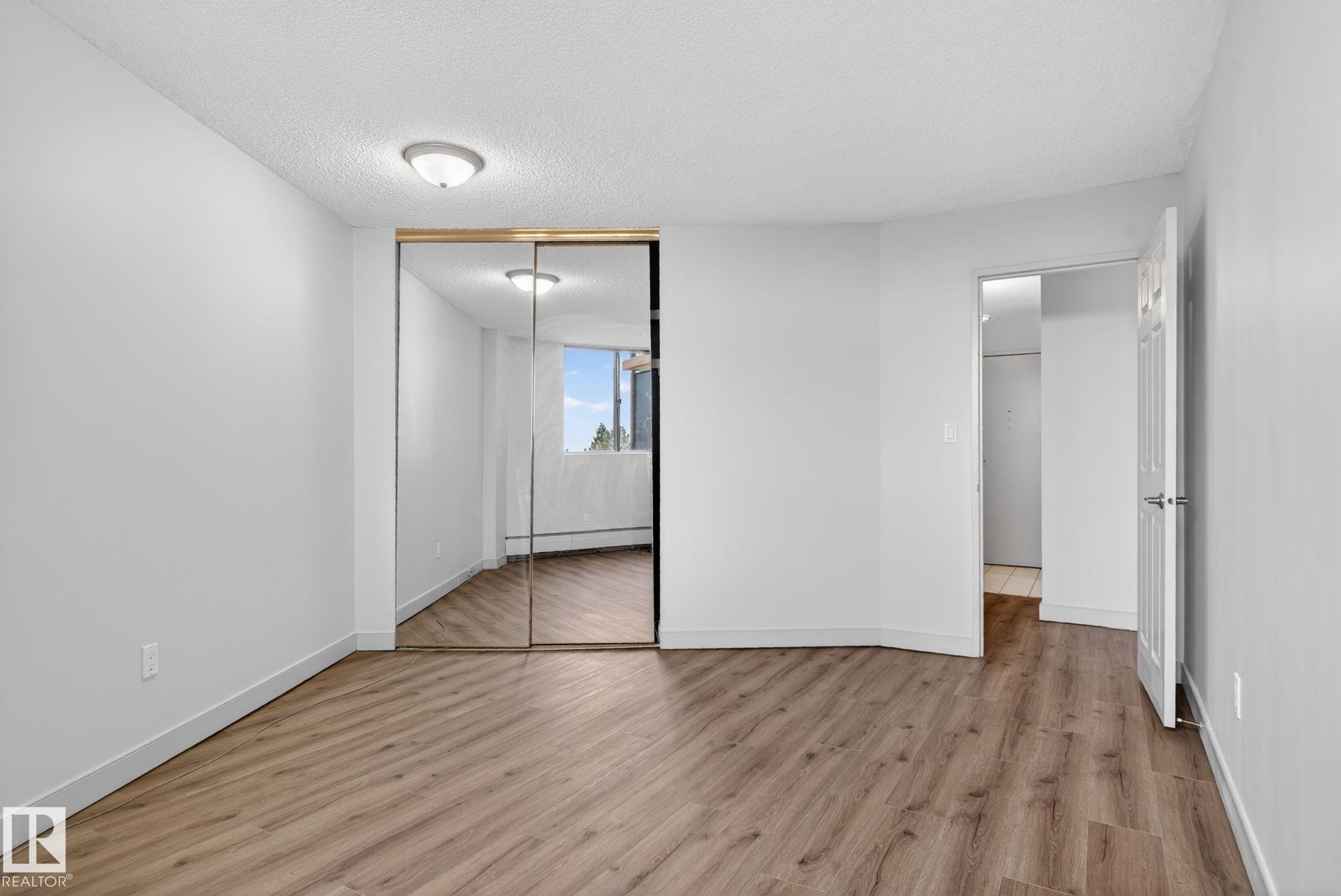 Interior space featuring wood-finish flooring, white painted walls, and a ceiling-mounted light fixture - #412 13910 Stony Plain Rd Nw, Edmonton, AB - Indoor Photo Showing Other Room