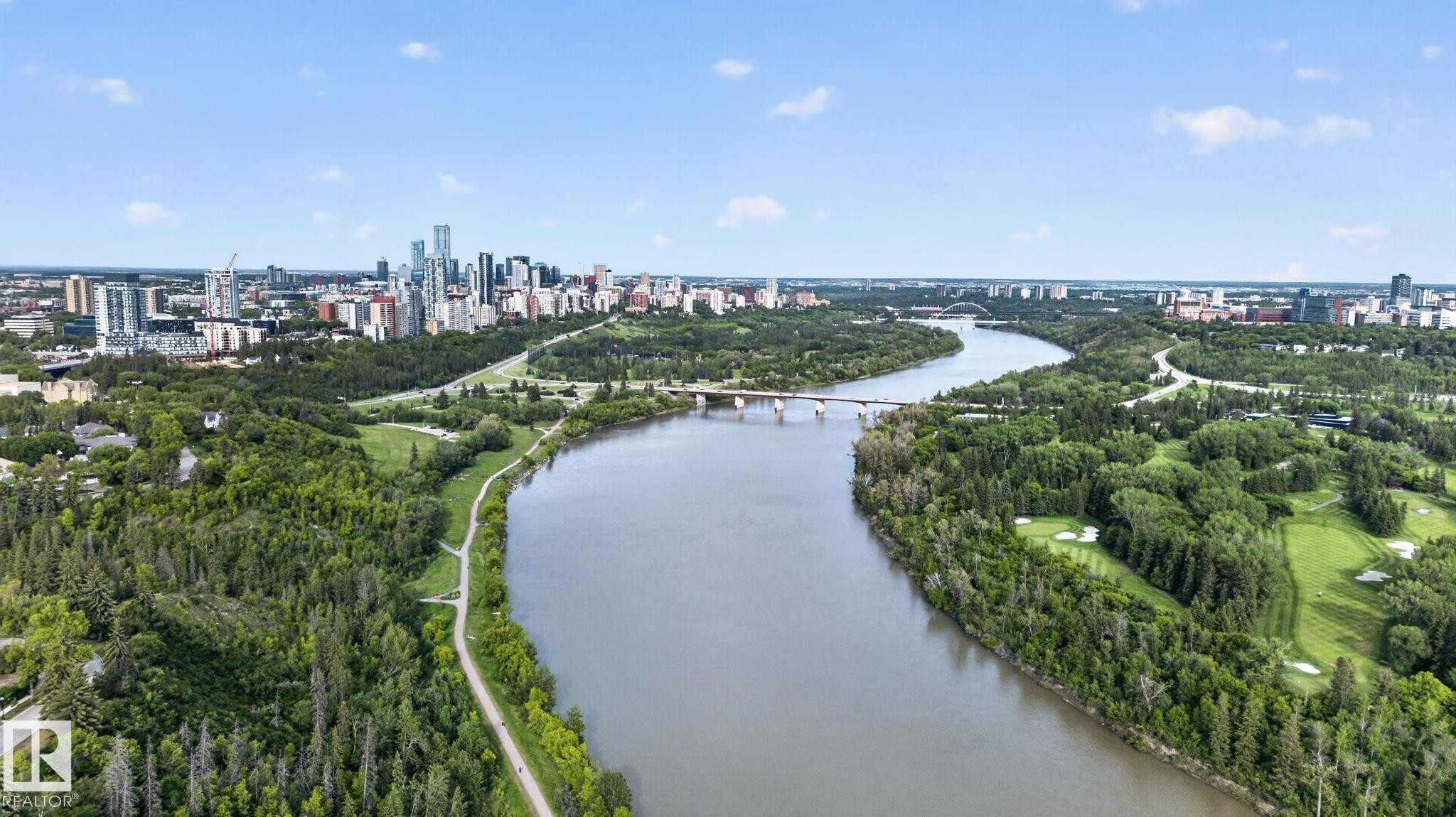 Riverfront cityscape with a prominent bridge, surrounded by extensive green spaces and dense tree coverage - #412 13910 Stony Plain Rd Nw, Edmonton, AB - Outdoor With Body Of Water With View