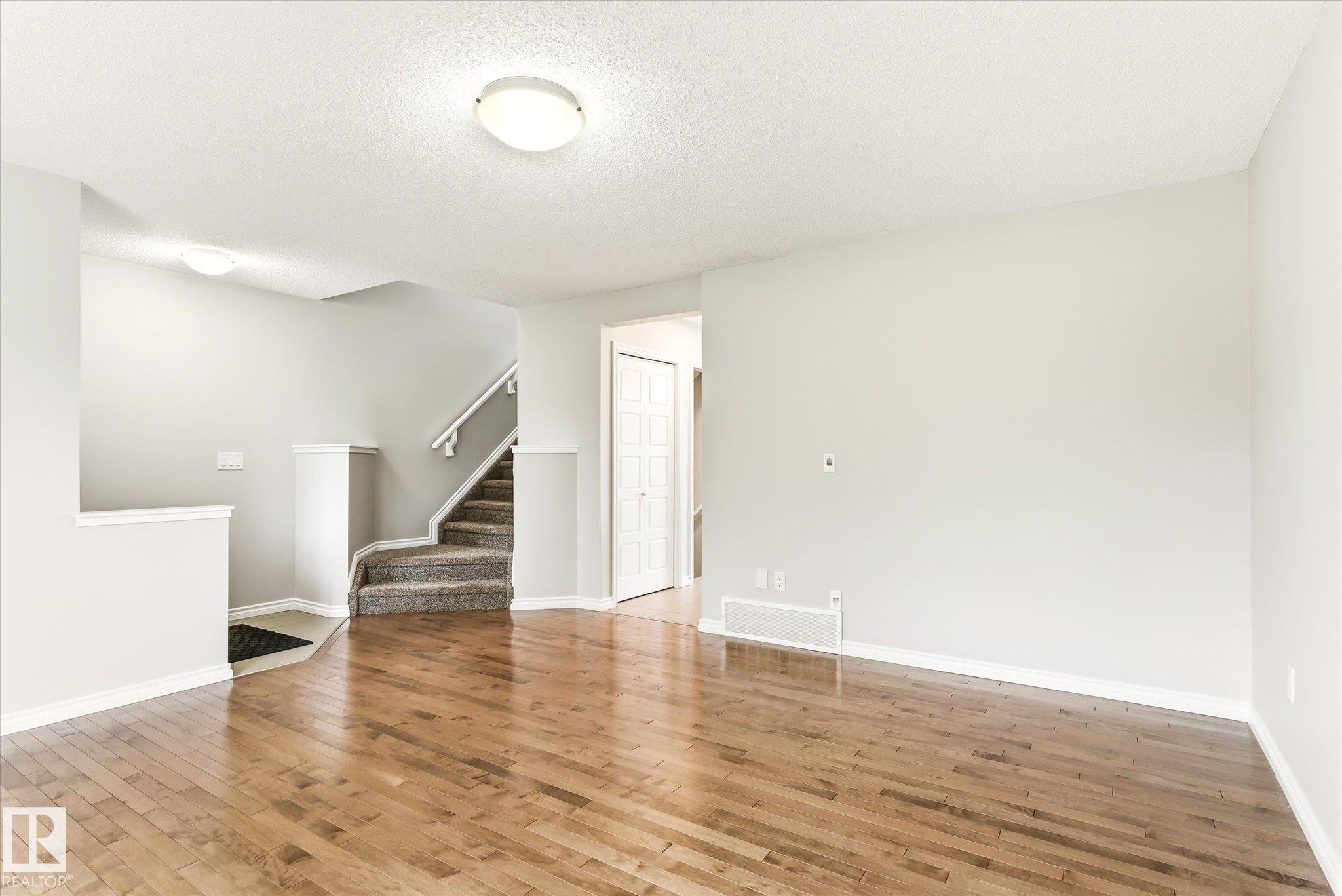 Hardwood-style flooring throughout a spacious room with light-toned walls - 9039 219 Street, Edmonton, AB