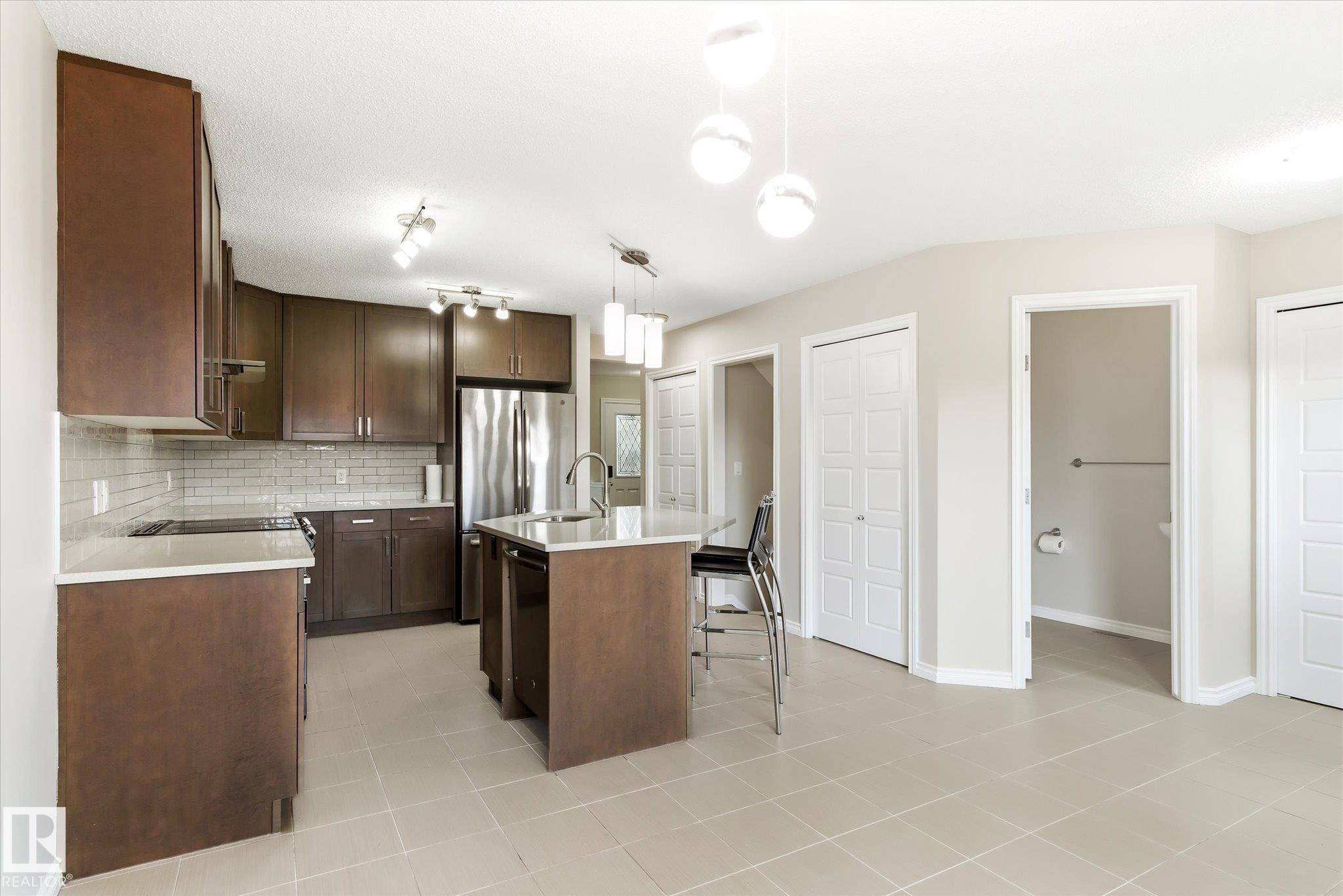 Modern kitchen featuring rich wood-finish cabinetry, white subway tile backsplash, stainless steel appliances, and a central island with a sink and pendant lighting - 9039 219 Street, Edmonton, AB
