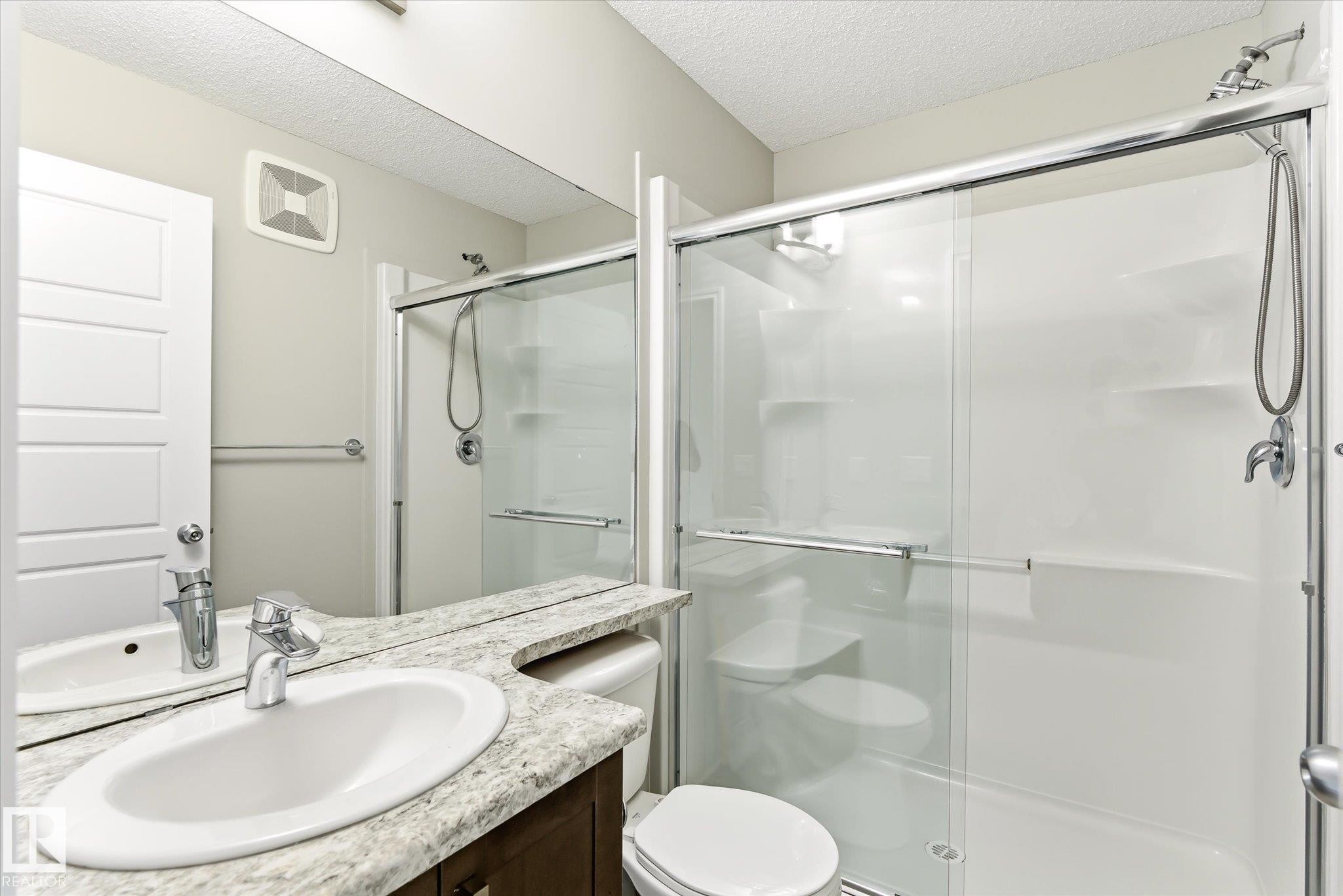 Bathroom featuring a glass-enclosed shower with sliding doors, a vanity with an oval sink and chrome faucet, and a stone-finish countertop - 9039 219 Street, Edmonton, AB