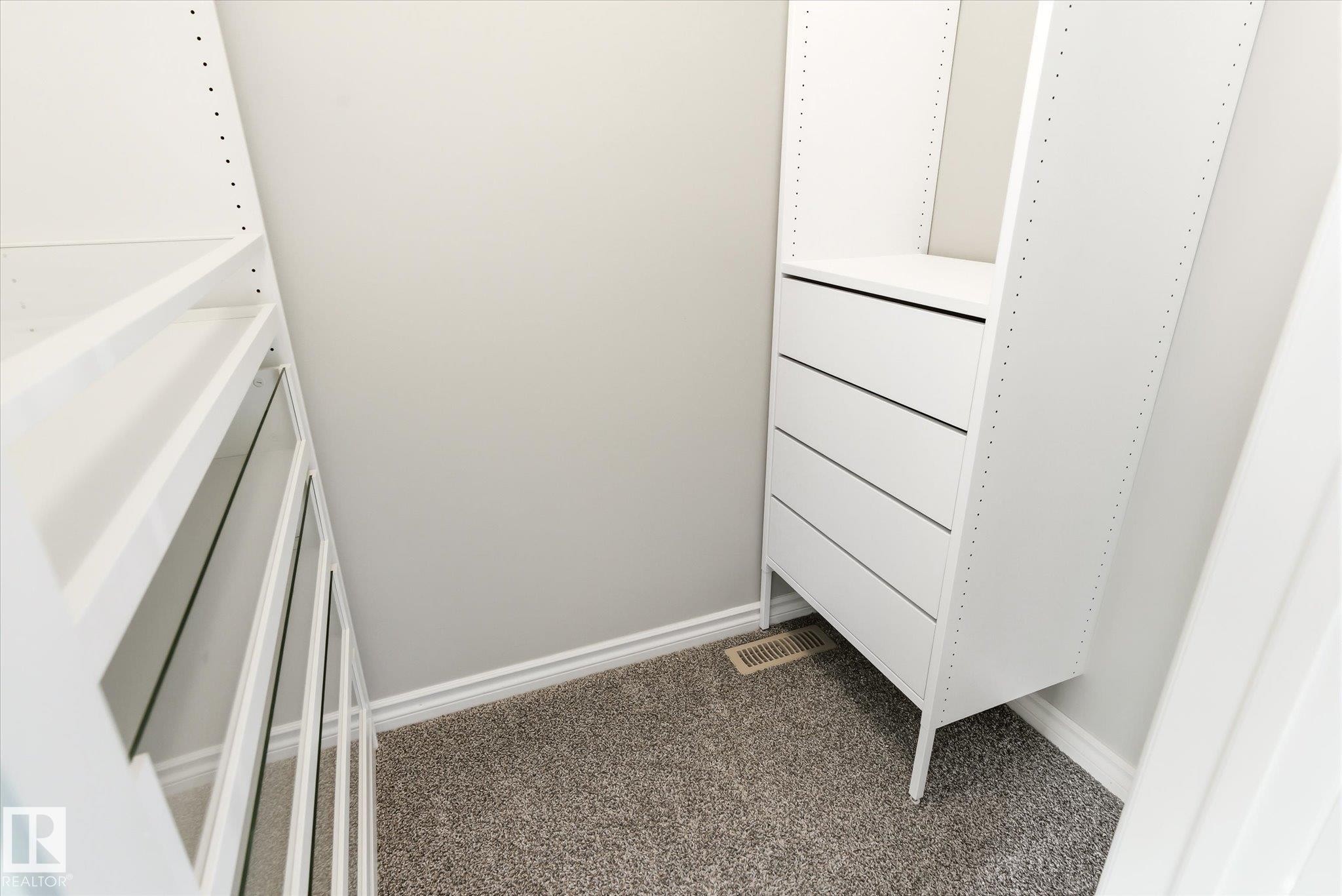 Custom closet organization system featuring white shelving, built-in drawers, gray carpet flooring, and white baseboard trim - 9039 219 Street, Edmonton, AB