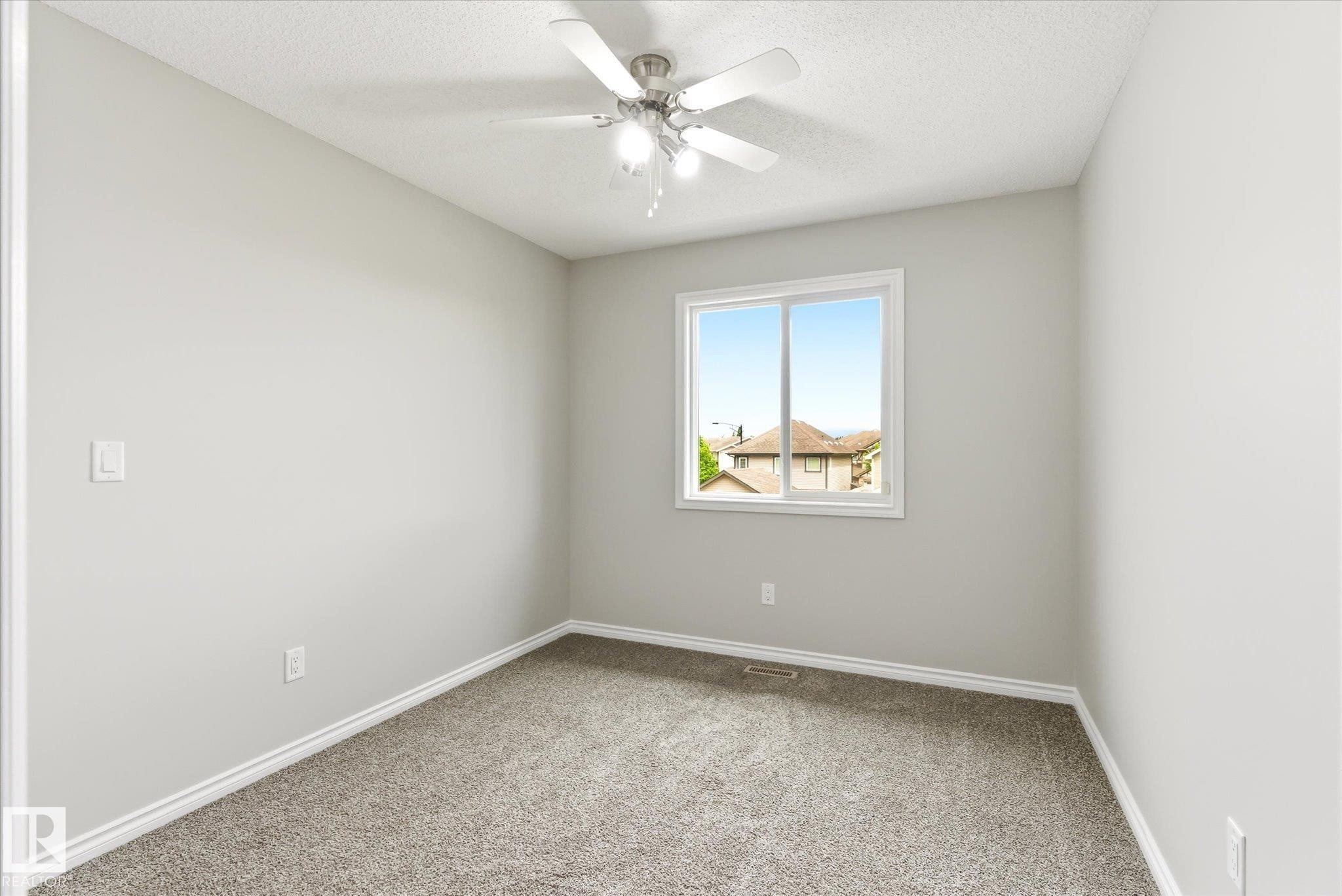 Neutral-toned room featuring a ceiling fan with integrated lighting, a window with a white frame, and gray carpeting - 9039 219 Street, Edmonton, AB