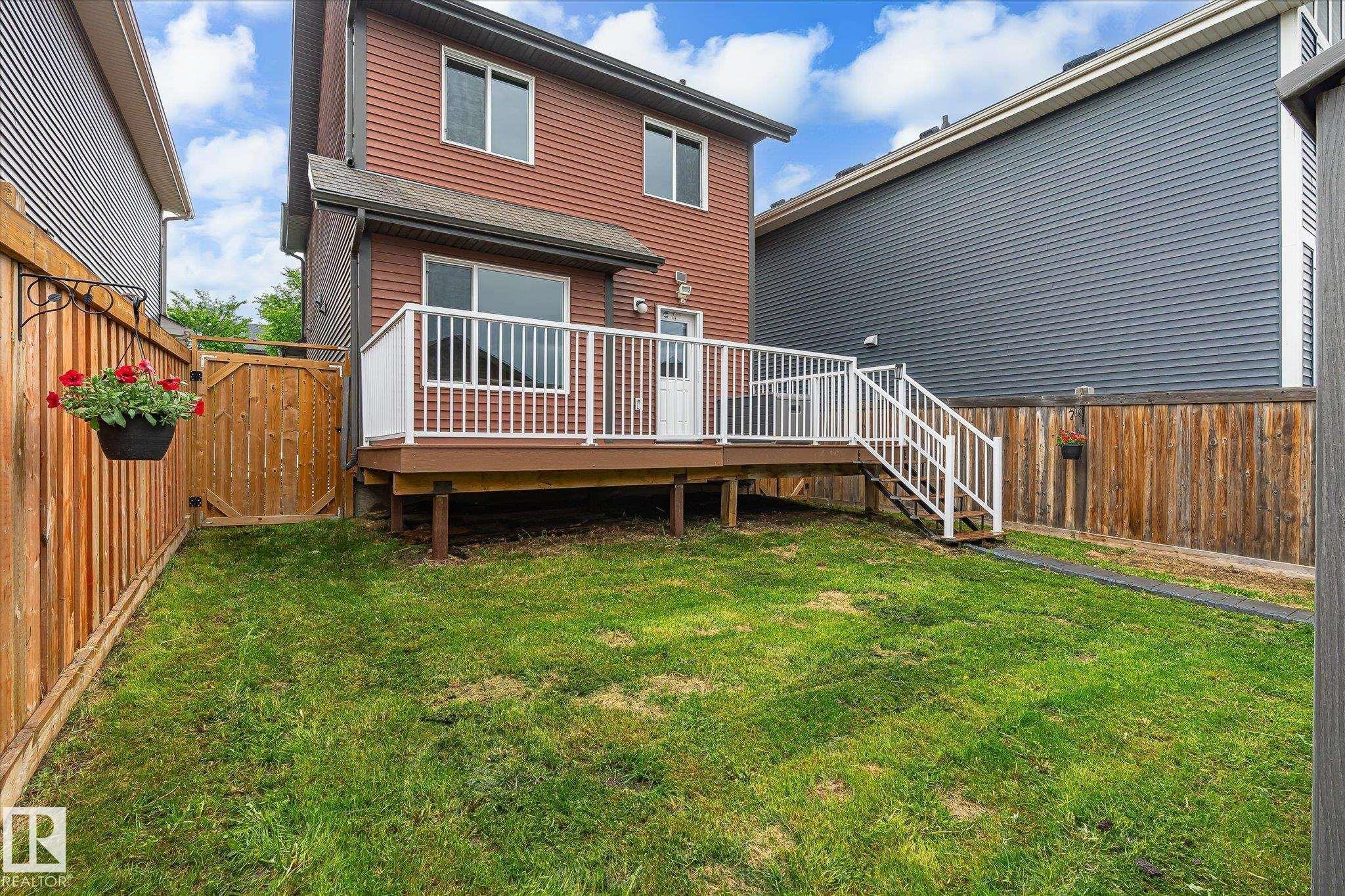 Rear exterior featuring a spacious wooden deck with white railings, steps to a grassy yard, and a full-height privacy fence - 9039 219 Street, Edmonton, AB