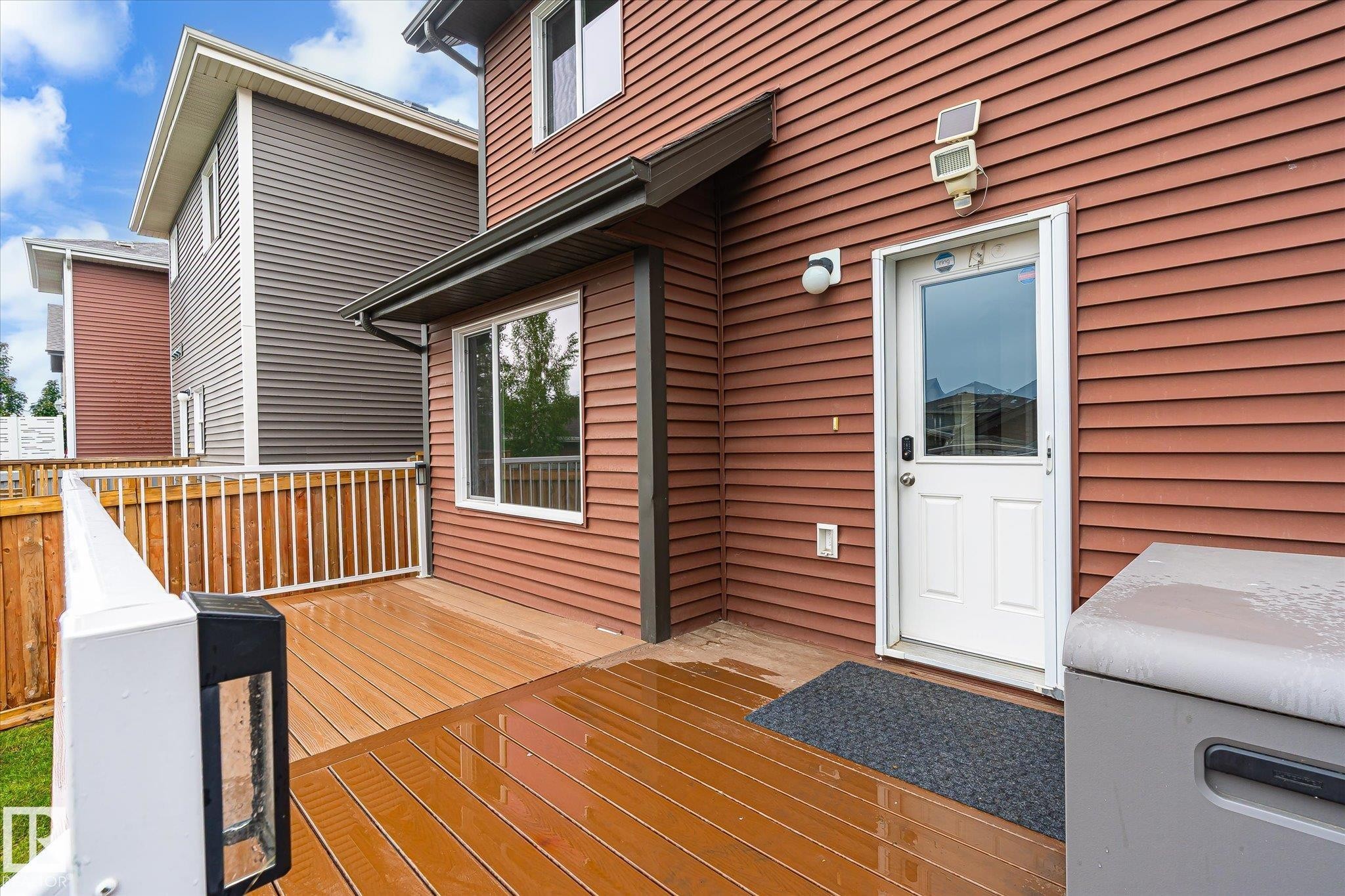 Wood-finish composite deck with white railings and privacy fencing, featuring a rear entry door with an integrated window, and a wall-mounted light fixture - 9039 219 Street, Edmonton, AB