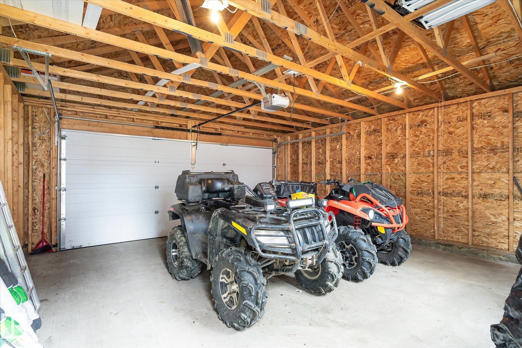 Spacious garage featuring exposed wood beam ceiling, concrete flooring, and a large white sectional garage door - 9039 219 Street, Edmonton, AB