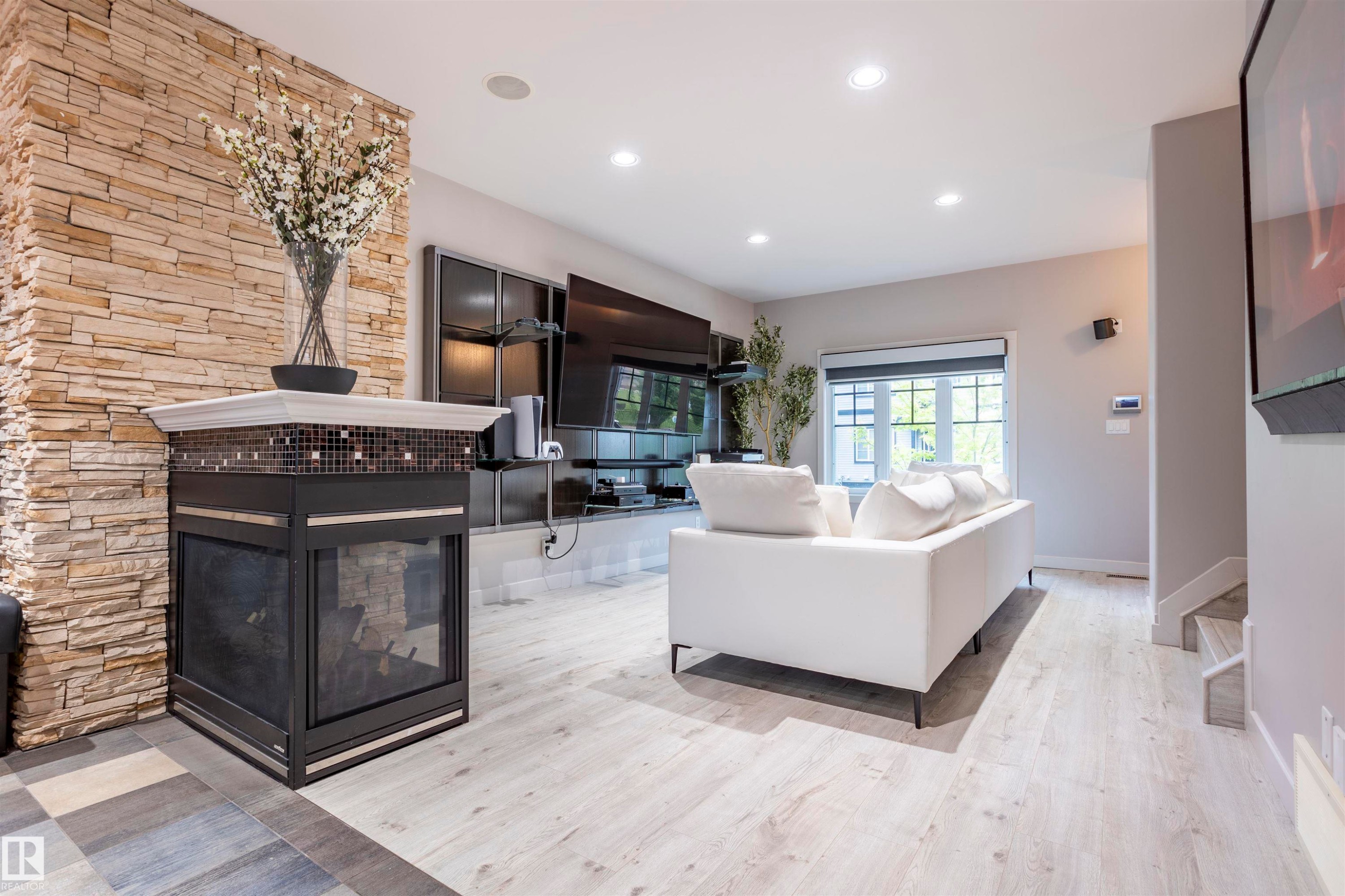 Living area featuring a stone accent wall, a fireplace with a tiled mantel, recessed lighting, and wood-finish flooring - 4949 Terwillegar Common Nw, Edmonton, AB