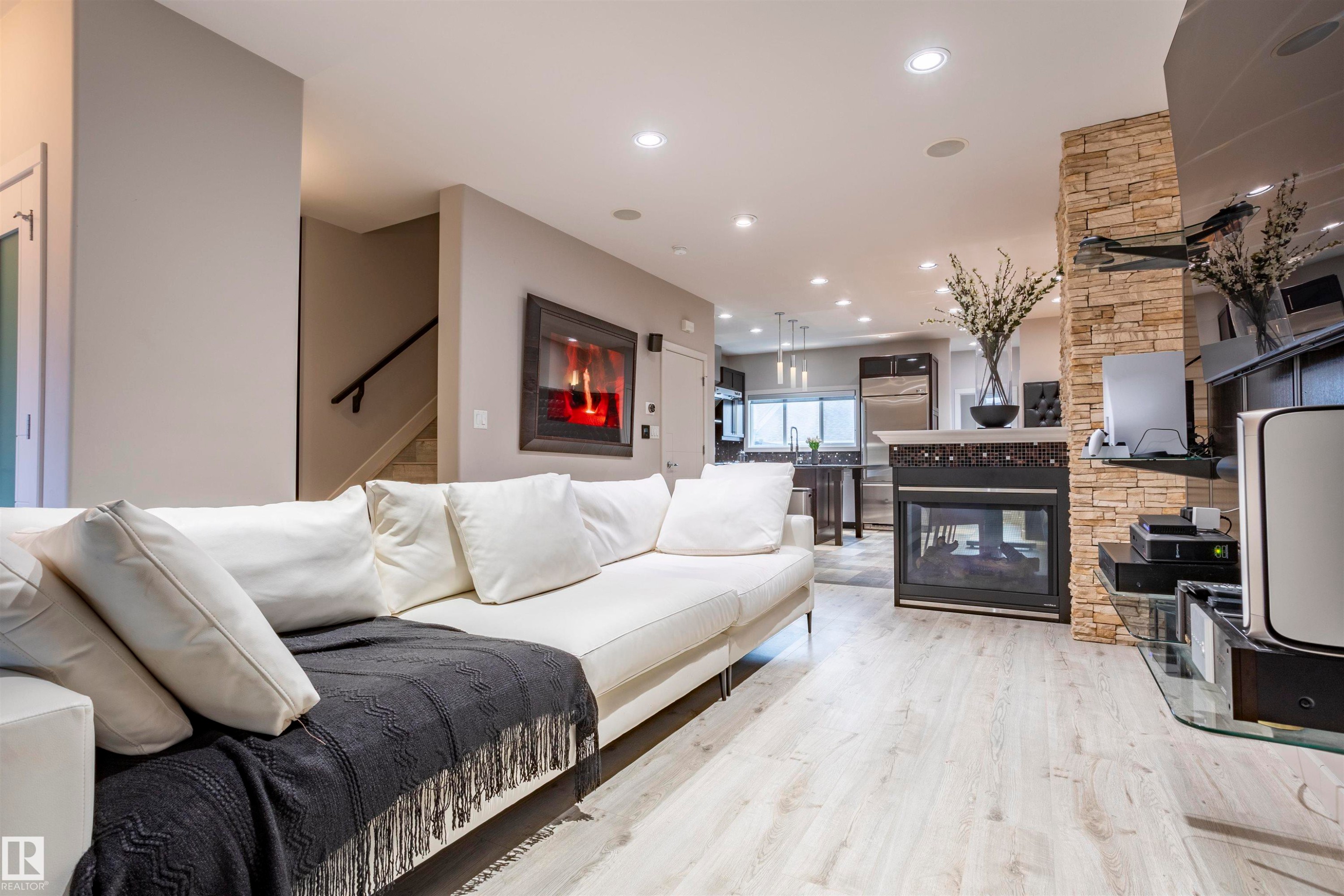 Open-concept living space featuring light wood-finish flooring, recessed lighting, and a stone-clad fireplace - 4949 Terwillegar Common Nw, Edmonton, AB