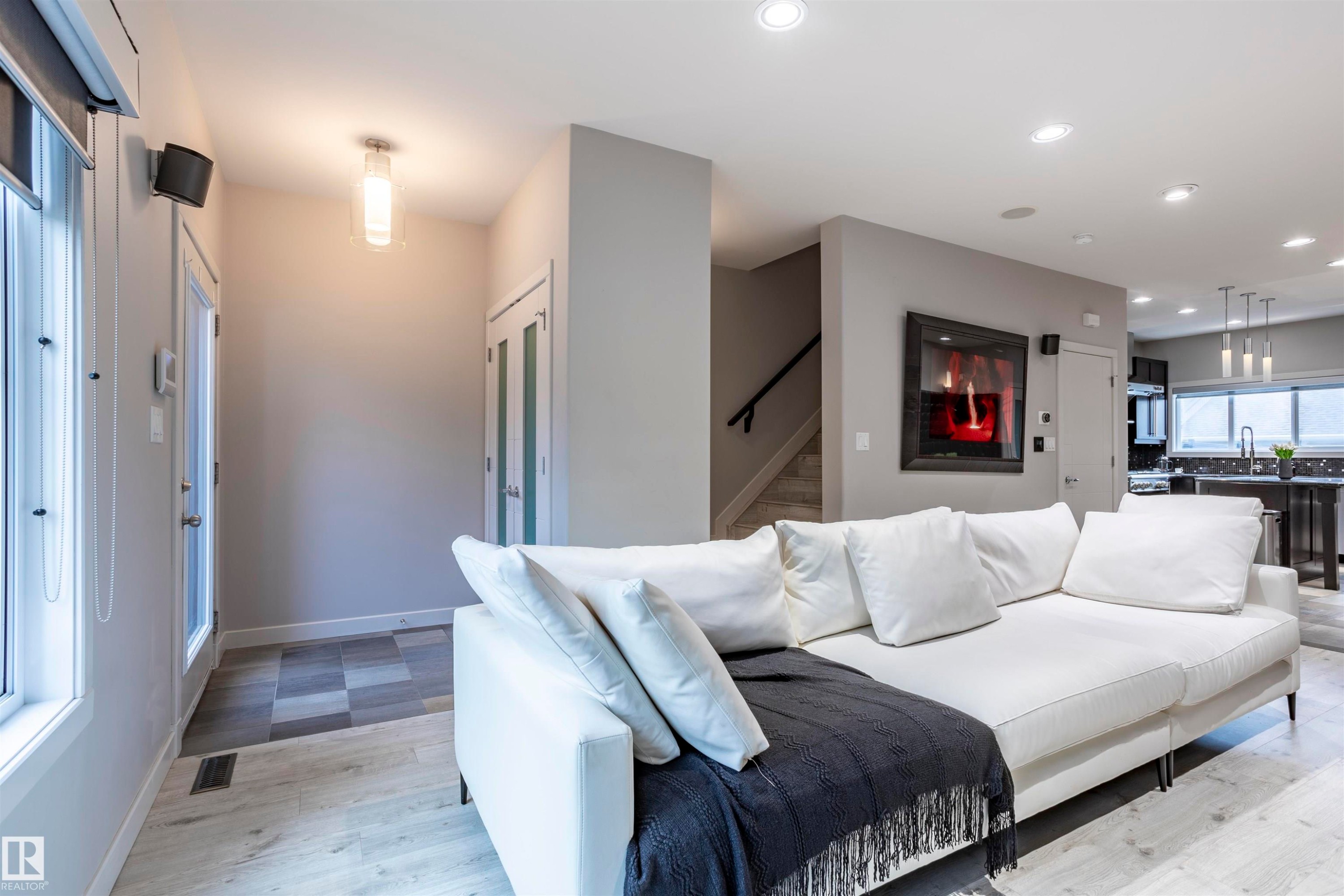 Open-concept living space featuring light wood-finish flooring, recessed lighting, and a modern wall-mounted fireplace - 4949 Terwillegar Common Nw, Edmonton, AB