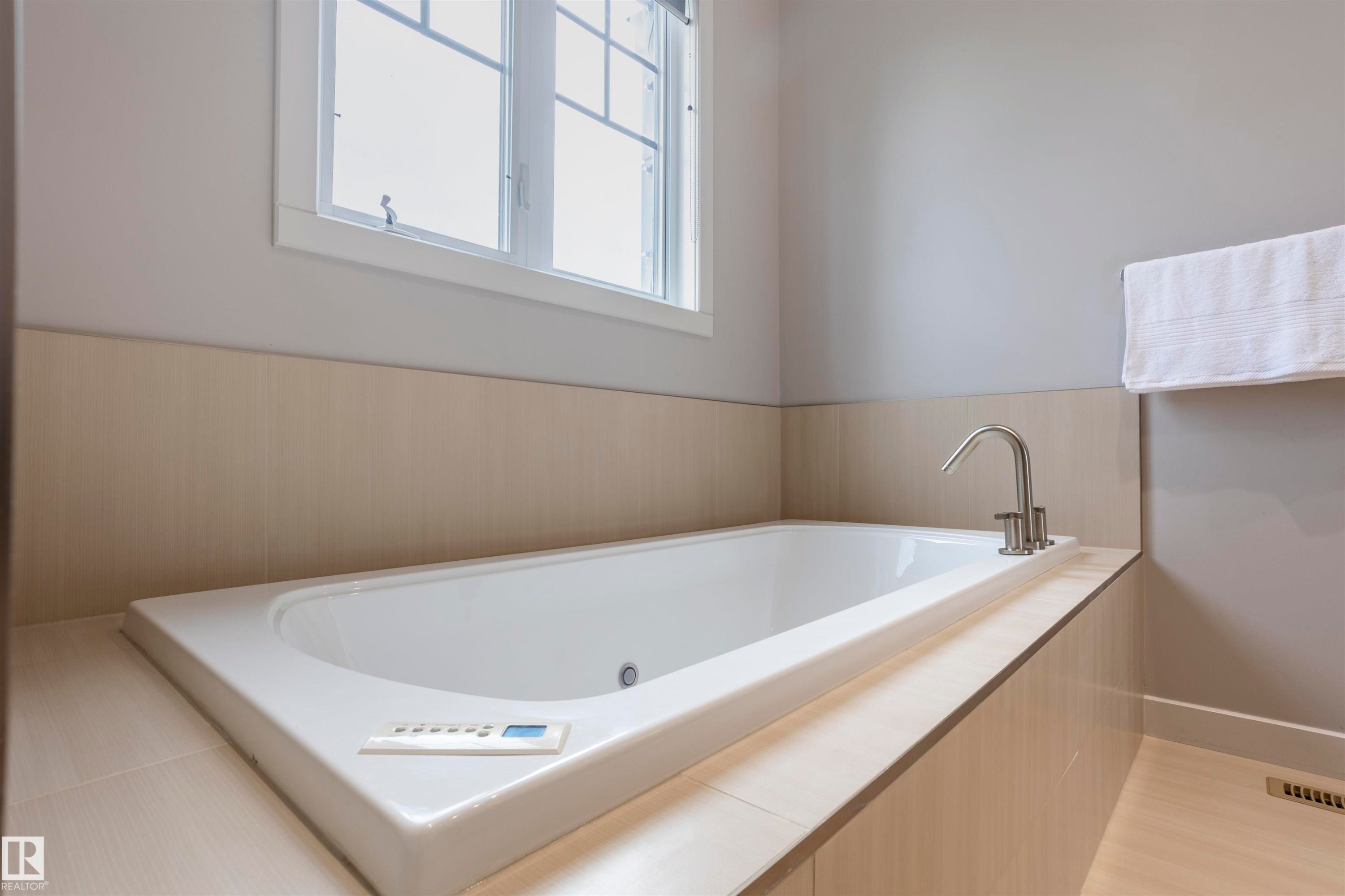 Built-in soaking tub with polished chrome fixtures, integrated control panel, and a light wood-finish surround - 4949 Terwillegar Common Nw, Edmonton, AB