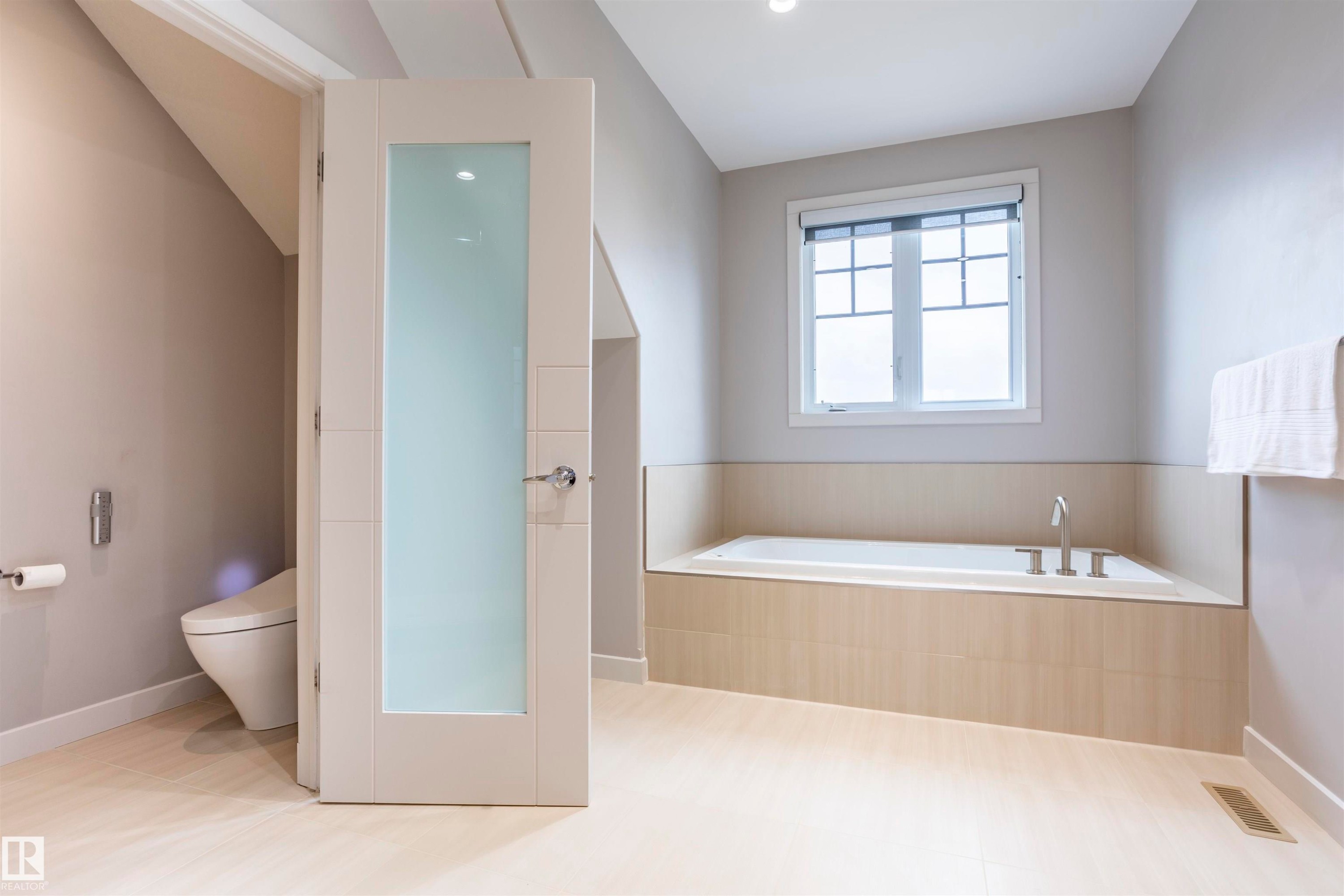 Soaking tub with built-in surround, frosted window, recessed lighting, wood-finish flooring, and a privacy-paneled door - 4949 Terwillegar Common Nw, Edmonton, AB