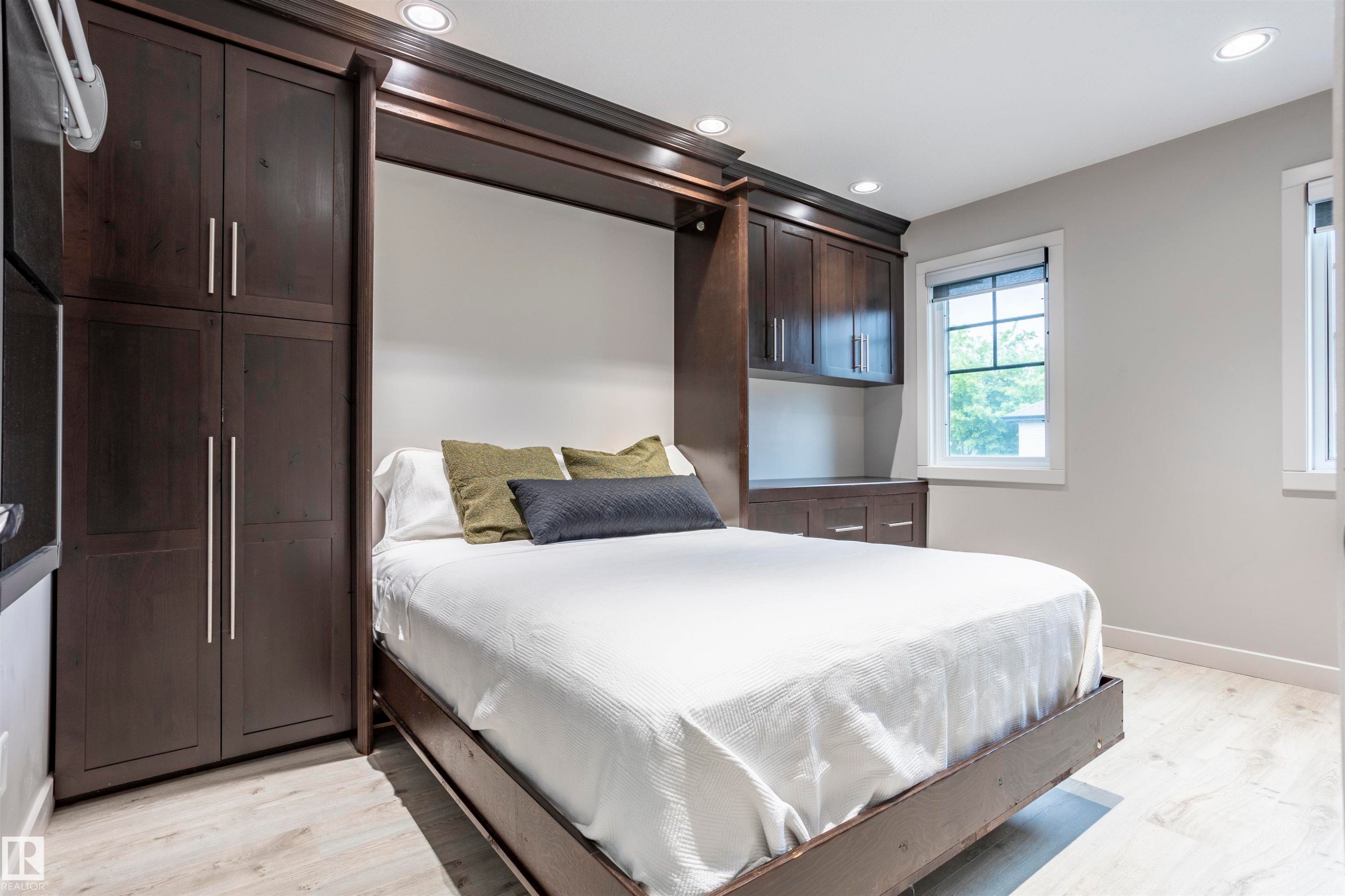 Integrated Murphy bed system featuring dark wood-finish cabinetry, recessed ceiling lighting, light wood-finish flooring, and white trim windows - 4949 Terwillegar Common Nw, Edmonton, AB