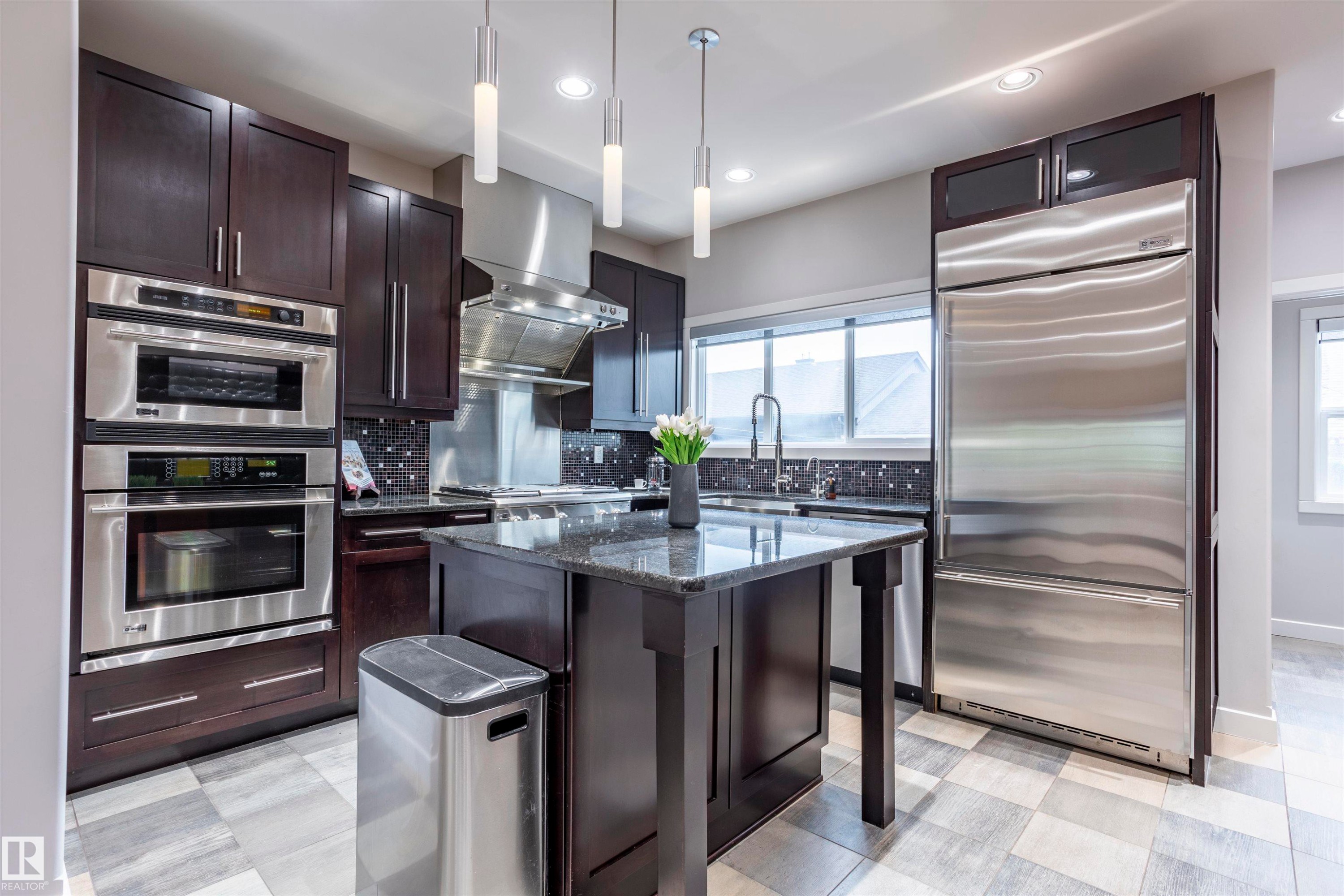 Gourmet kitchen with dark wood cabinetry, stainless steel appliances, granite countertops, and a central island - 4949 Terwillegar Common Nw, Edmonton, AB
