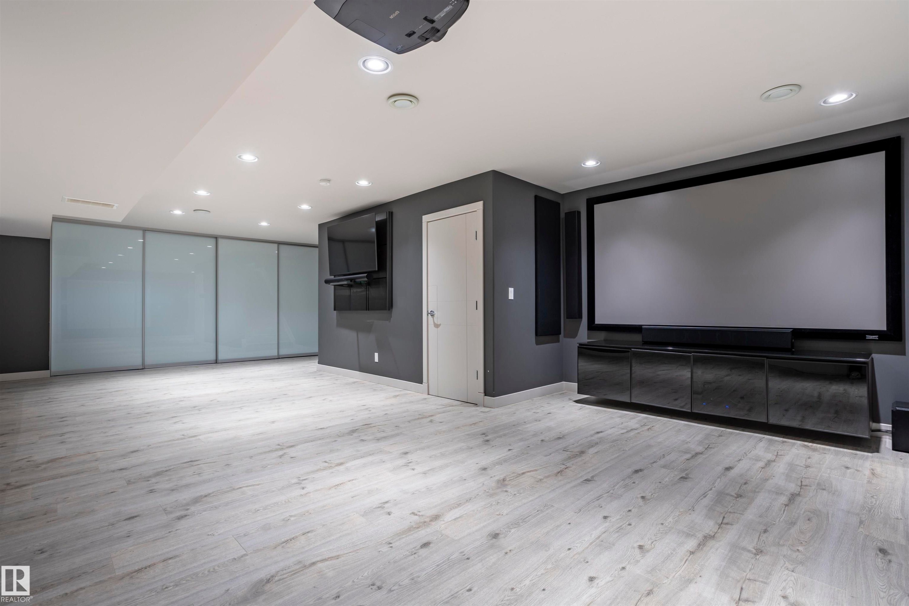 Spacious entertainment room featuring a large projection screen, recessed lighting, wood-finish flooring, and a wall-mounted media console - 4949 Terwillegar Common Nw, Edmonton, AB