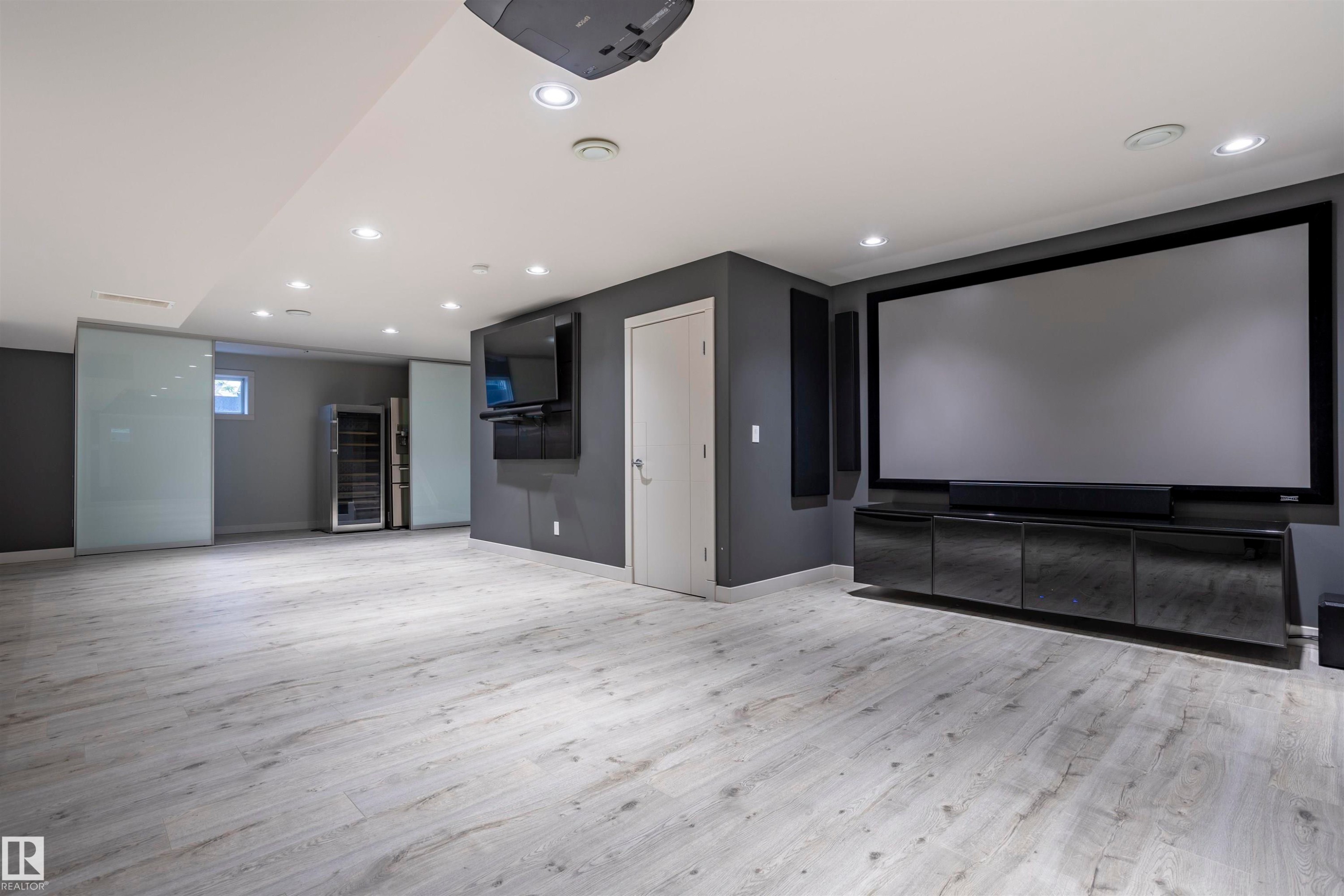 Entertainment space featuring a large projection screen, built-in media console, wood-finish flooring, recessed lighting, and sliding frosted glass panels - 4949 Terwillegar Common Nw, Edmonton, AB