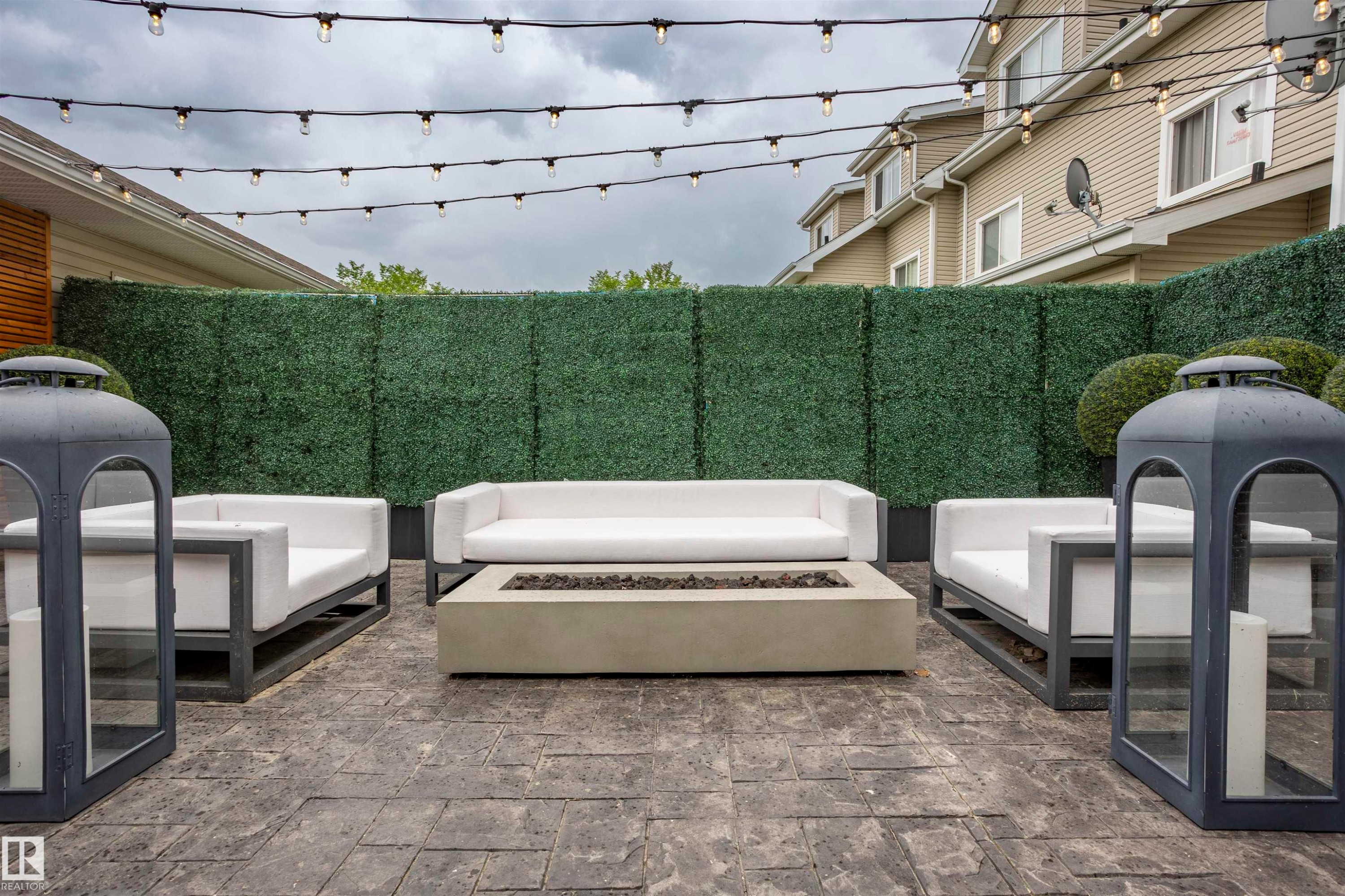 Expansive outdoor patio featuring stamped concrete flooring, a built-in fire pit, and a tall green privacy hedge - 4949 Terwillegar Common Nw, Edmonton, AB