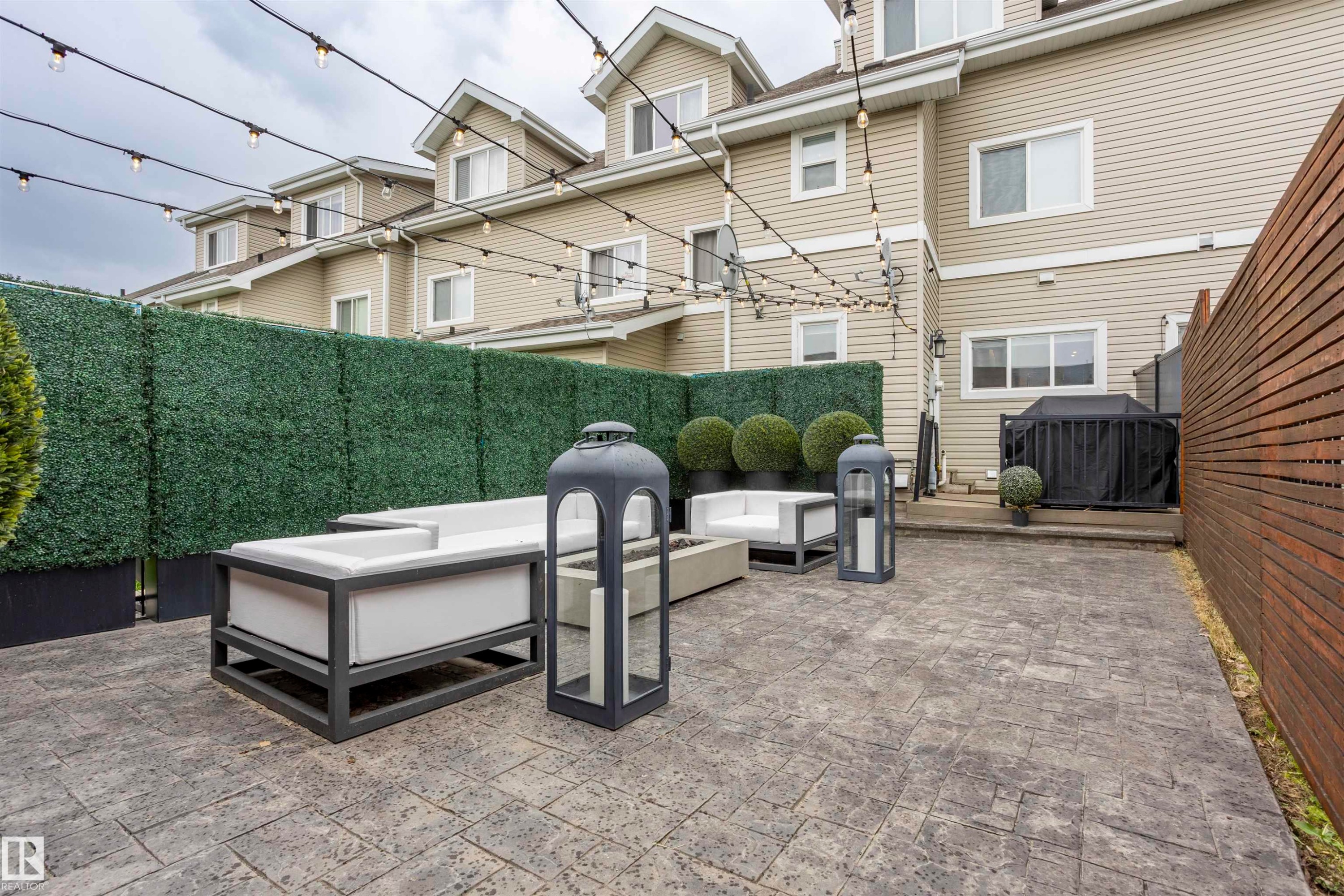 Expansive private patio featuring stamped concrete flooring, a horizontal slat wood fence, and a faux hedge privacy screen - 4949 Terwillegar Common Nw, Edmonton, AB
