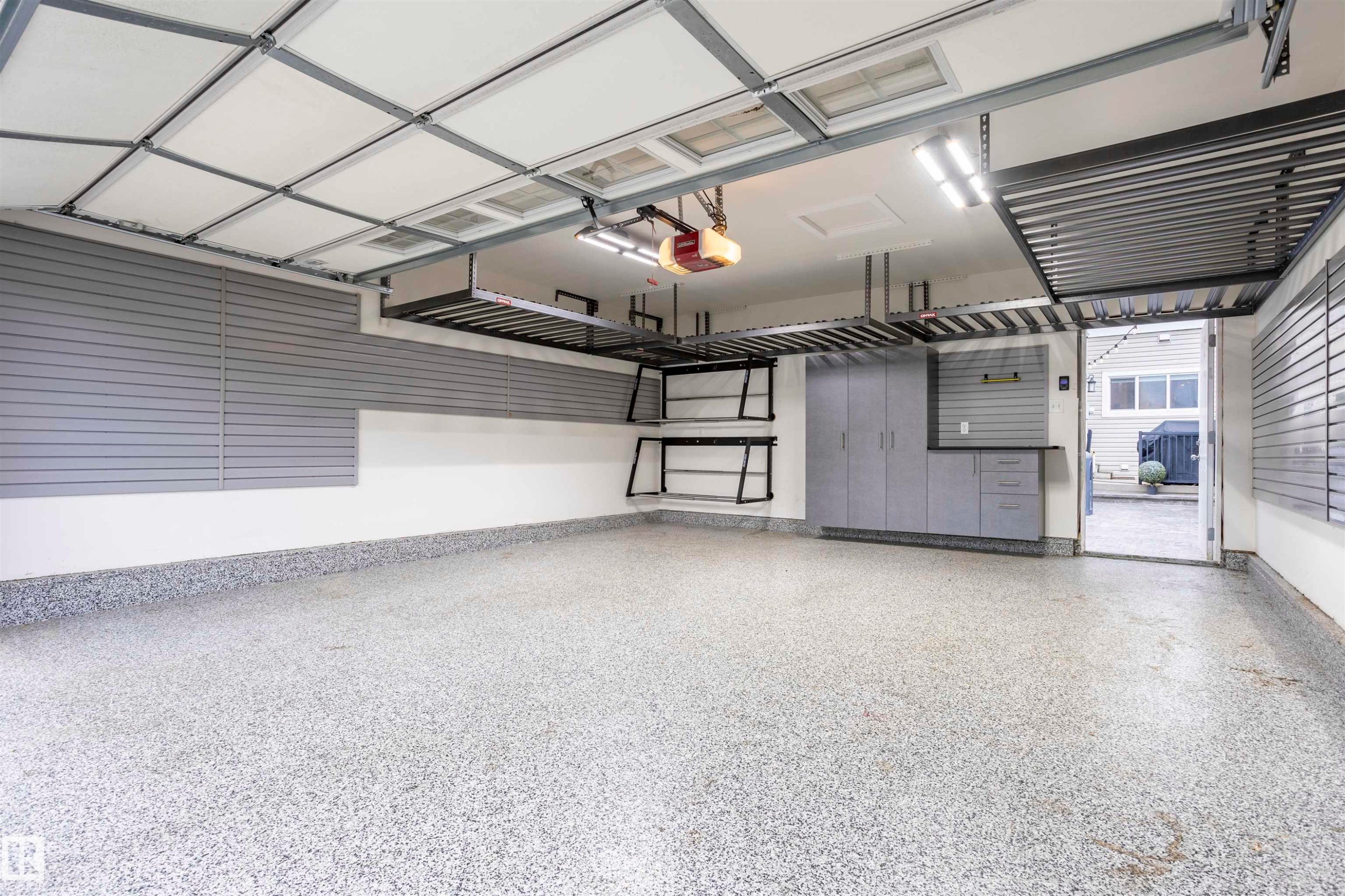 Spacious garage featuring a speckled epoxy floor, overhead storage racks, integrated slatwall panels, built-in cabinetry, and LED lighting - 4949 Terwillegar Common Nw, Edmonton, AB