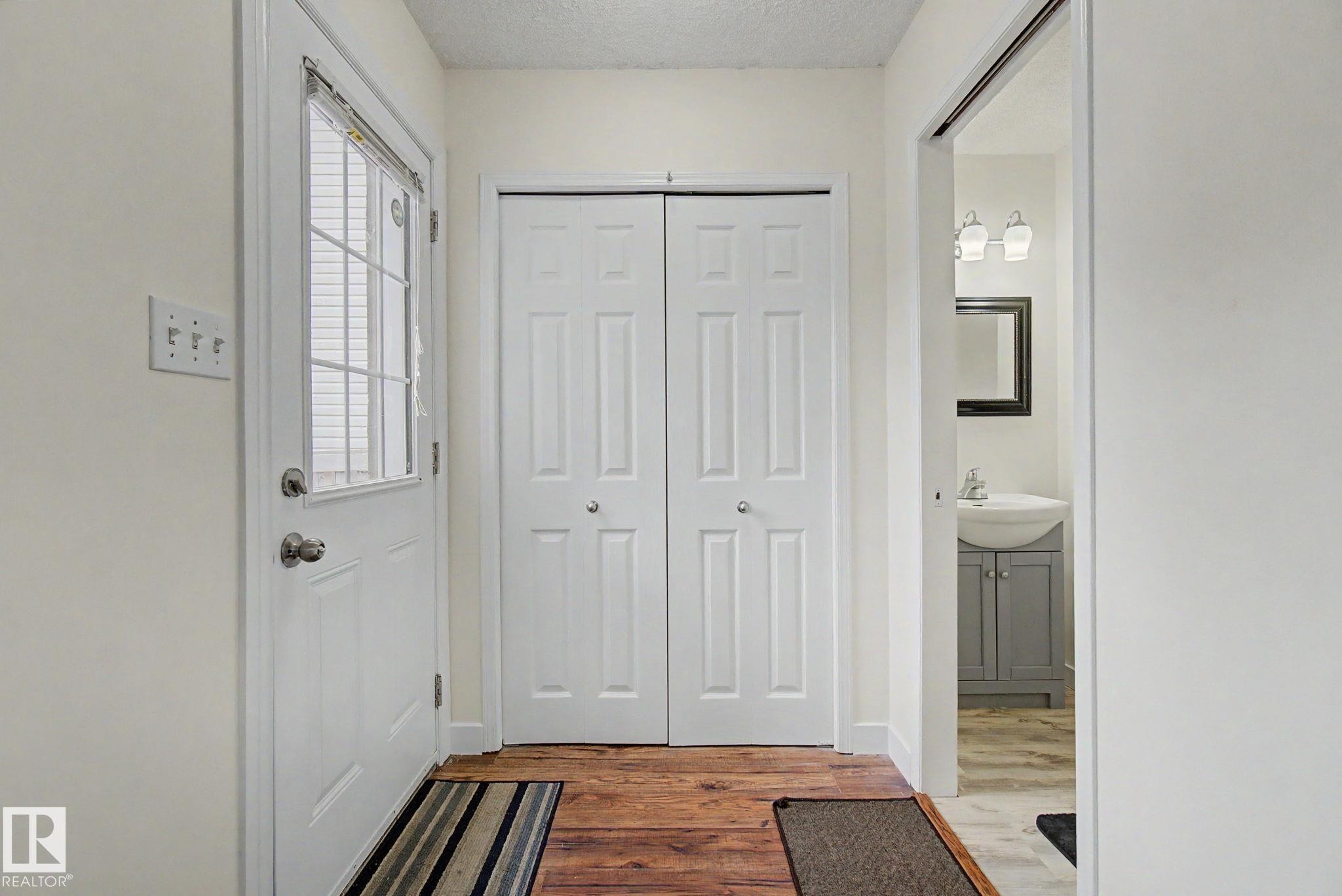 Entryway featuring wood-finish flooring, a white paneled door with an integrated window, bi-fold closet doors, and light-colored walls - 710 Glenwright Court, Edmonton, AB