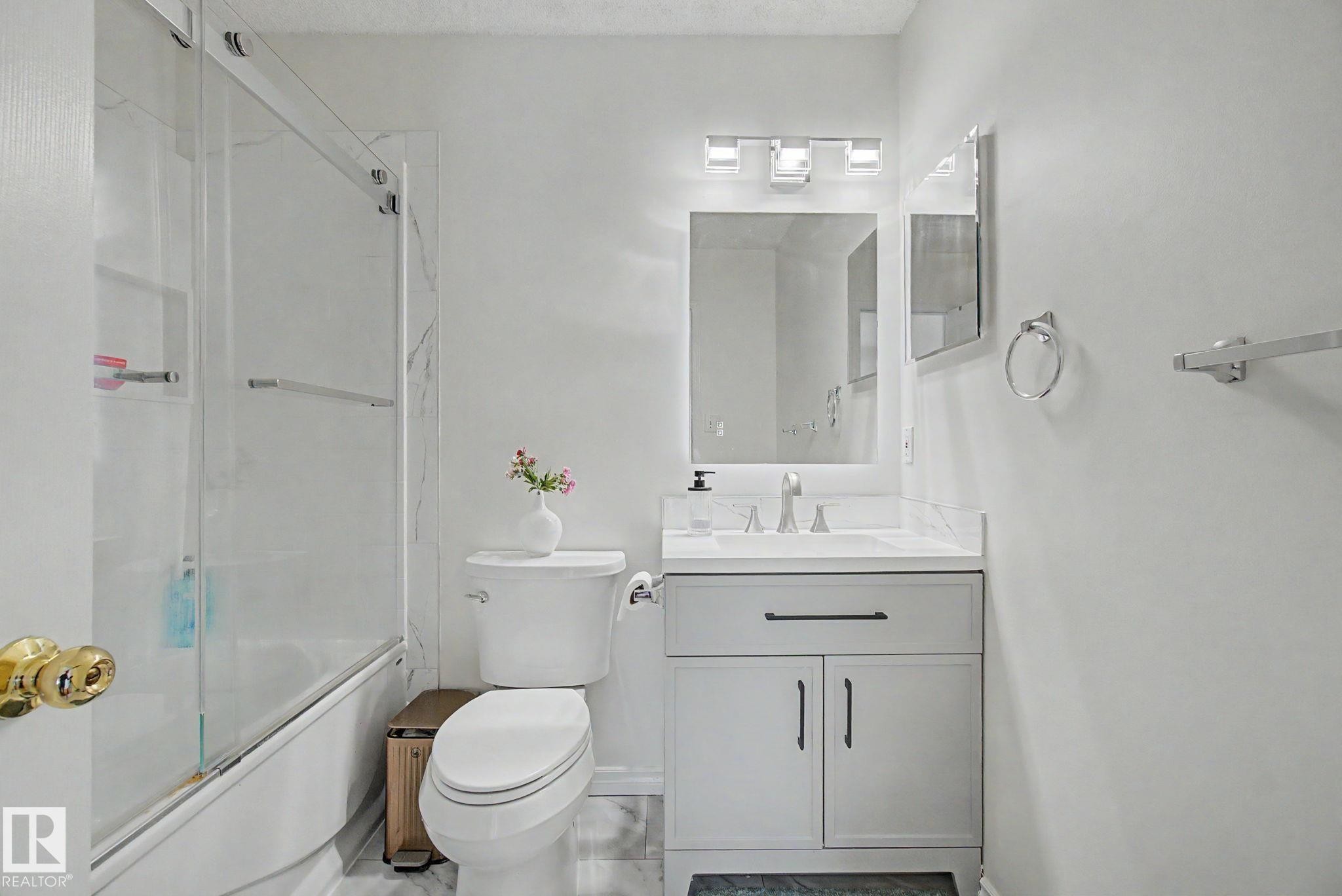 Bathroom featuring a single vanity with a white countertop and white cabinetry, a rectangular mirror, and a three-light vanity fixture - 710 Glenwright Court, Edmonton, AB