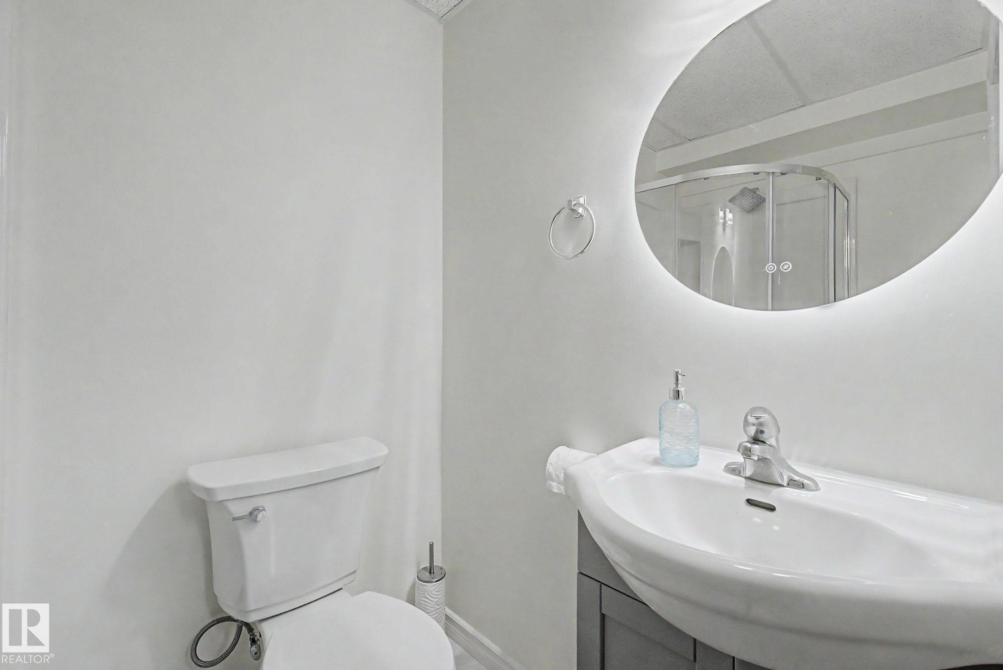 Contemporary bathroom vanity with integrated sink, chrome faucet, and backlit oval mirror - 710 Glenwright Court, Edmonton, AB