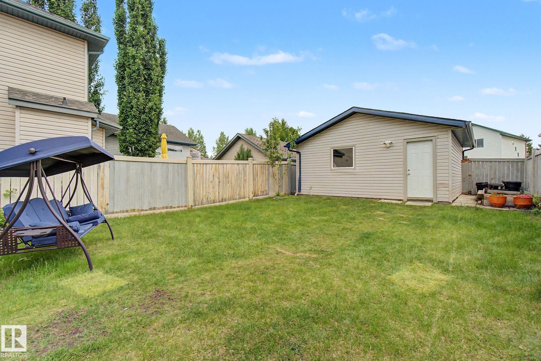 Expansive backyard featuring a detached garage with light-colored siding, a white service door, and a single window - 710 Glenwright Court, Edmonton, AB