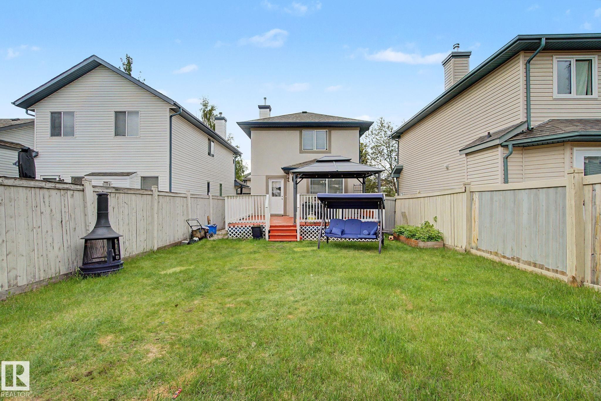 Expansive backyard with a manicured lawn, full wood fencing, and a multi-level deck featuring white railings and red-painted stairs - 710 Glenwright Court, Edmonton, AB