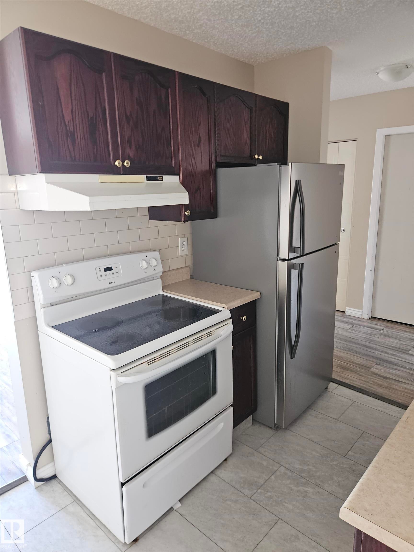 Kitchen with dark wood cabinetry, white subway tile backsplash, white electric range, stainless steel refrigerator, and light-toned countertops - #301 10615 110 Street Nw Nw, Edmonton, AB - Indoor Photo Showing Kitchen