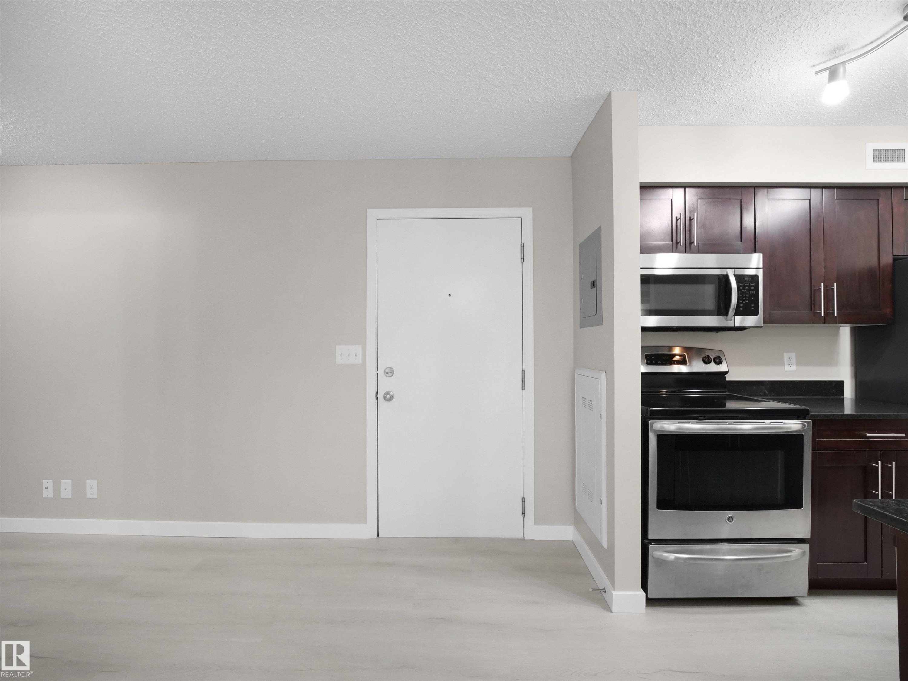 Modern kitchen featuring dark wood cabinetry, stainless steel appliances, black countertops, and a built-in microwave - 220 12035 22 Avenue, Edmonton, AB