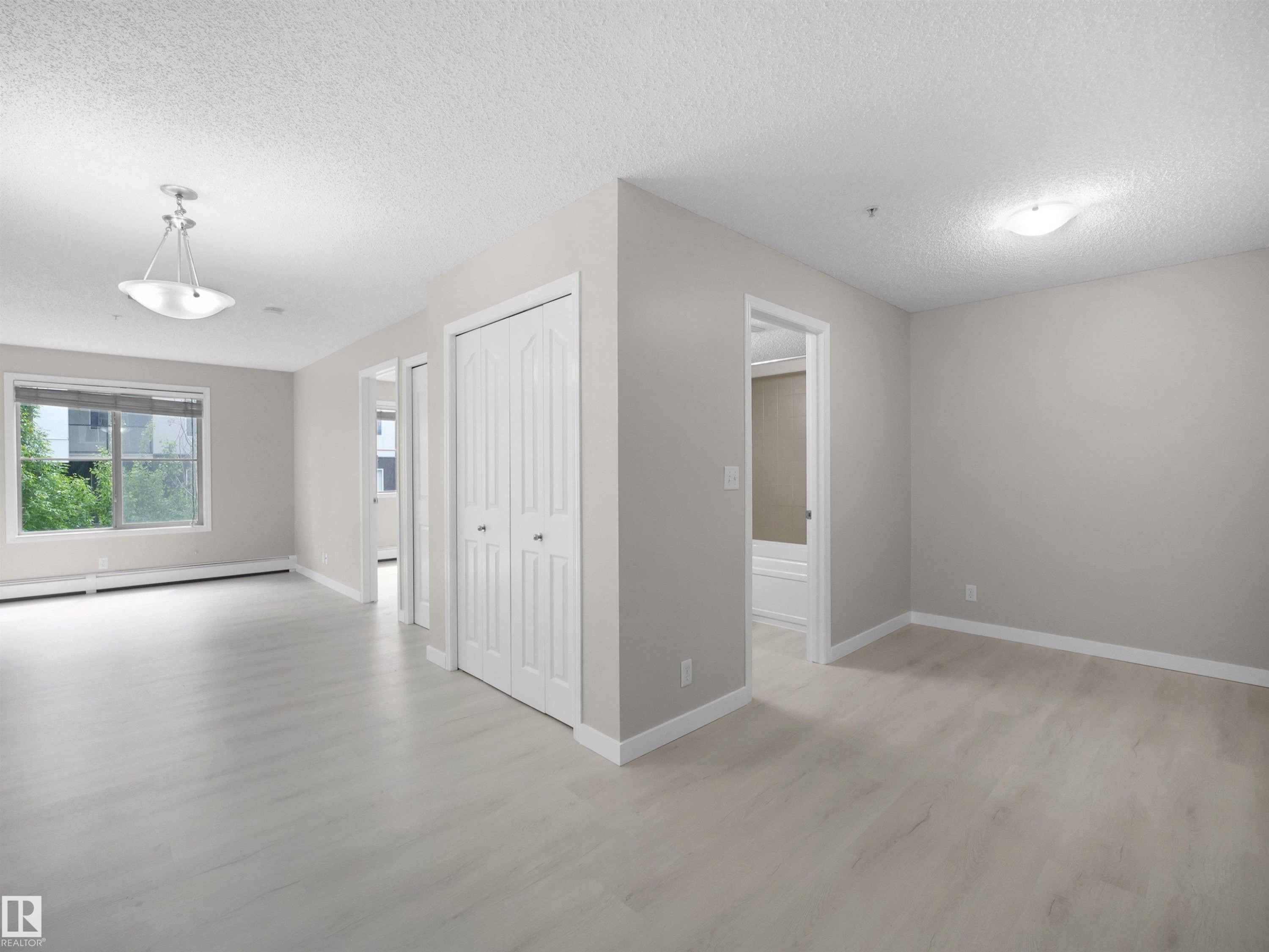 Bright interior space featuring light wood-finish flooring, neutral wall paint, and white trim throughout - 220 12035 22 Avenue, Edmonton, AB