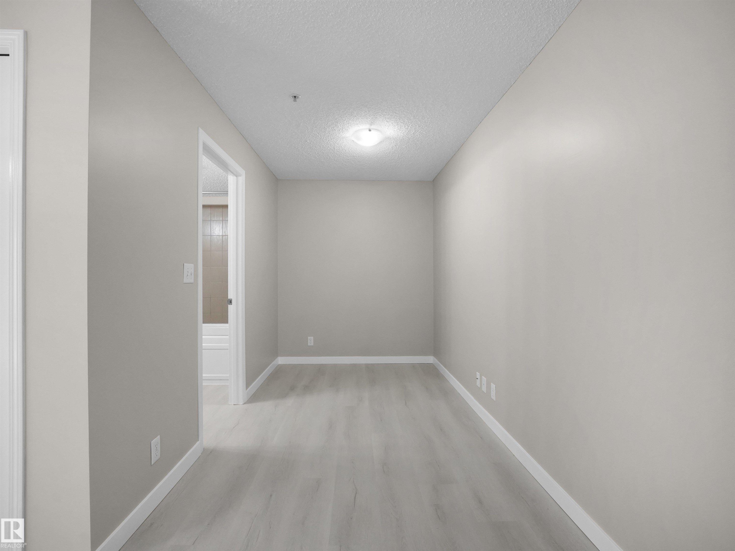 Neutral-toned hallway featuring light wood-finish flooring, white baseboards, and a flush-mount ceiling light - 220 12035 22 Avenue, Edmonton, AB