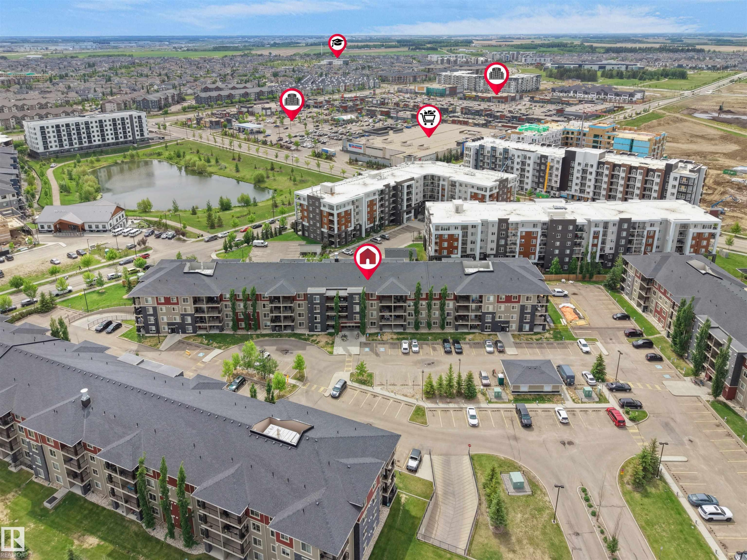 Aerial overview of an urban residential community featuring multi-story buildings with balconies, extensive parking areas, and surrounding green spaces - 220 12035 22 Avenue, Edmonton, AB