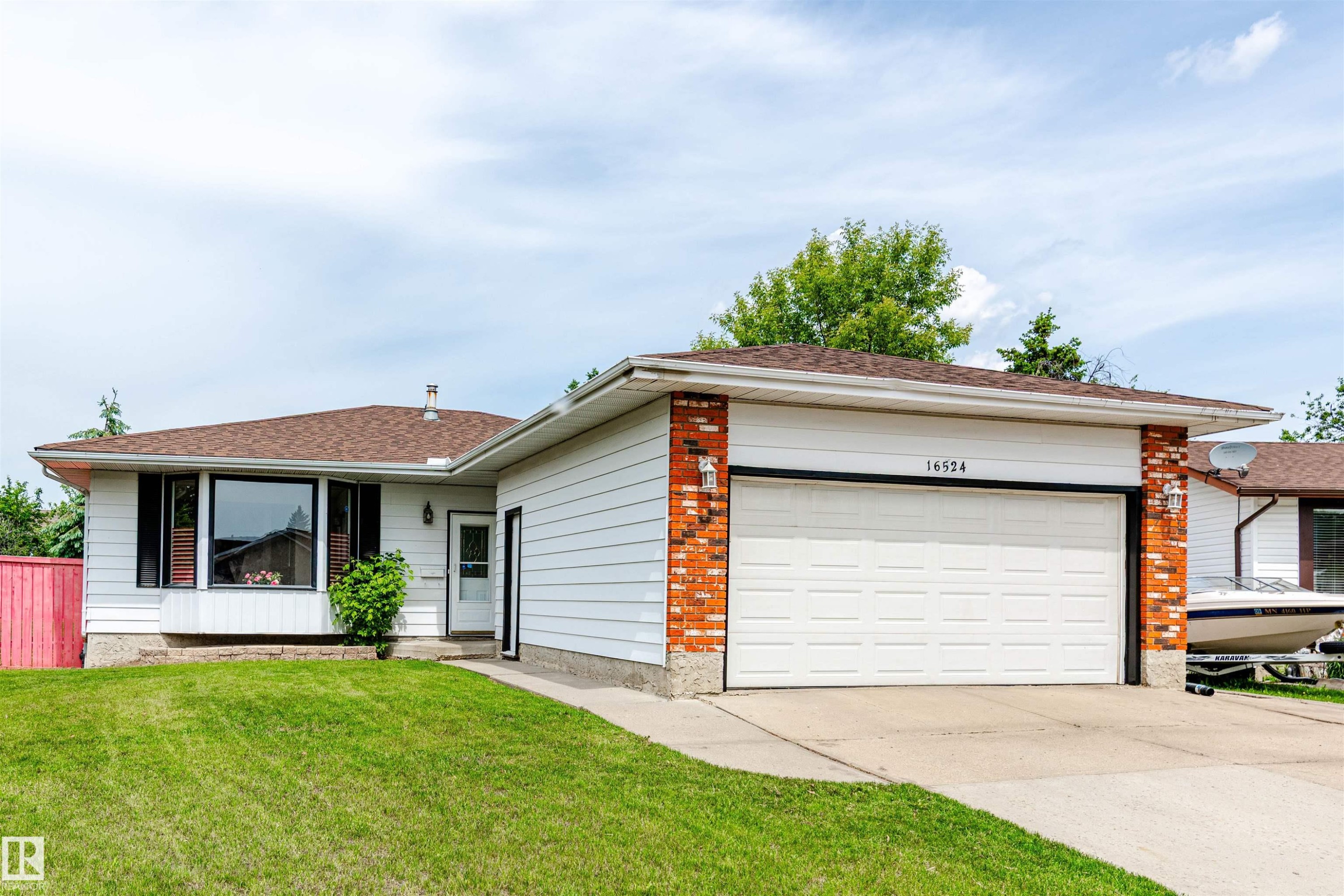 Single-story residence featuring a two-car garage with a white sectional door, brick accents, and white siding - 16524 116 Street, Edmonton, AB