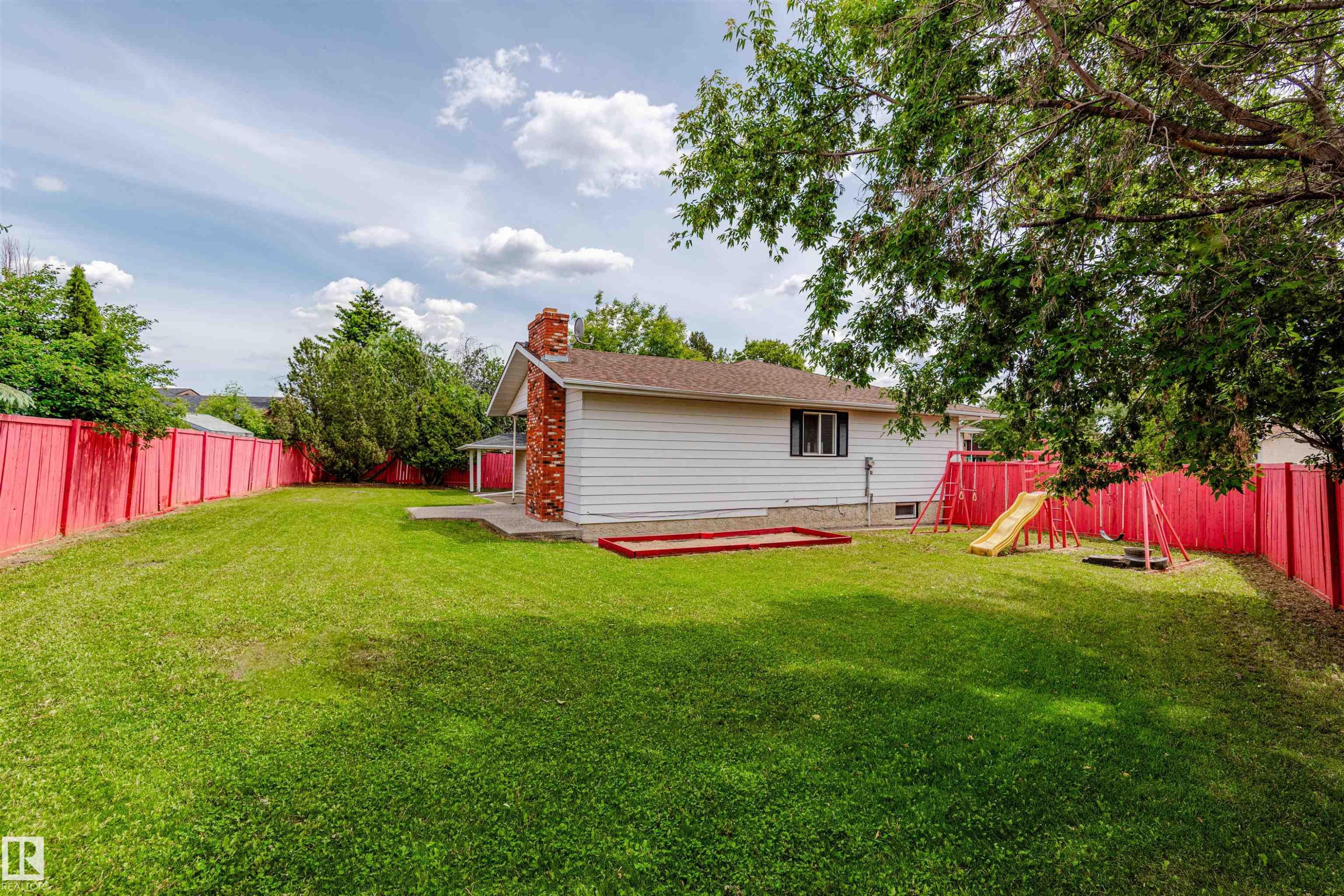 Expansive backyard featuring a manicured lawn, vibrant red privacy fencing, and mature trees - 16524 116 Street, Edmonton, AB