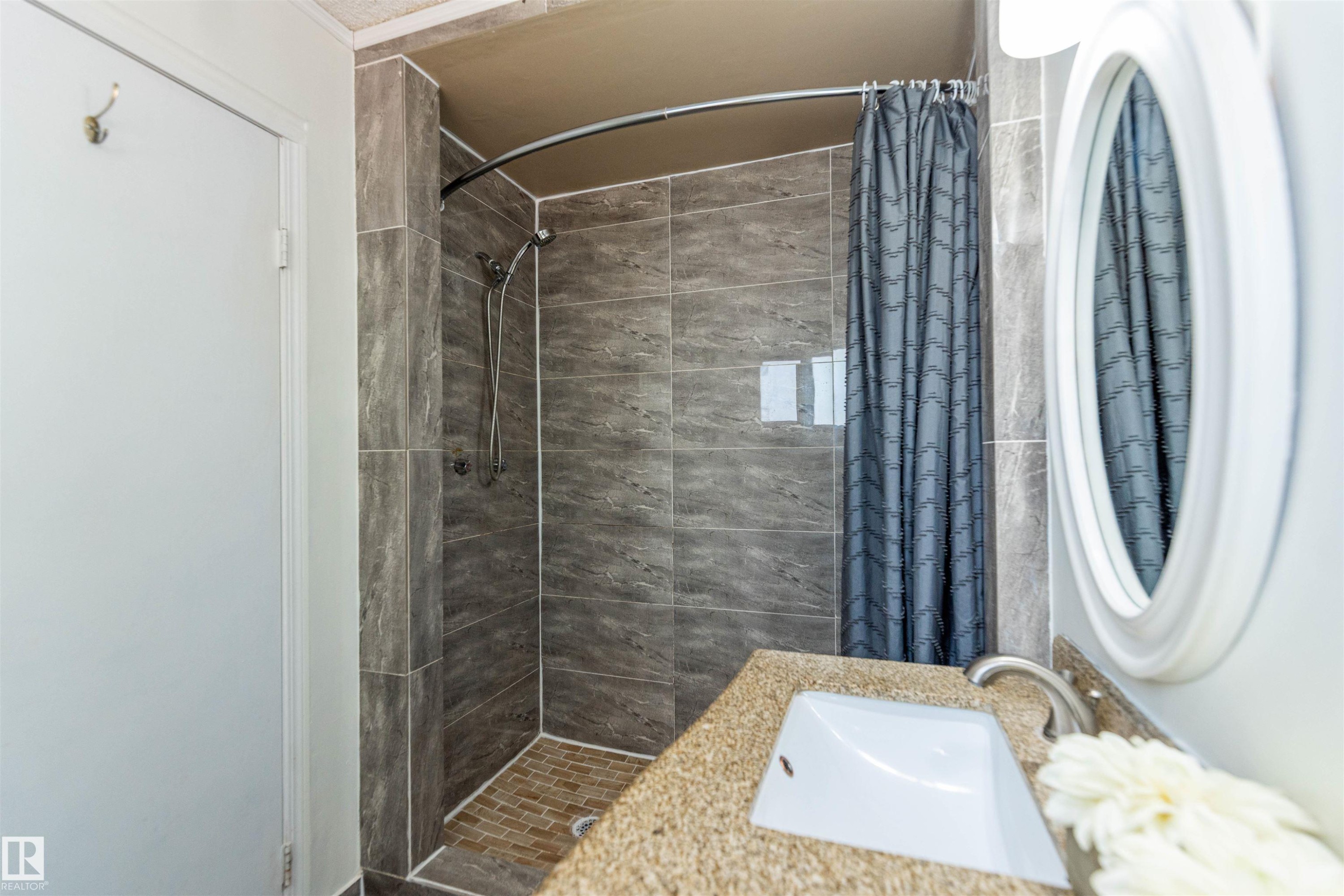 Bathroom featuring a tiled shower with a curved rod, a vanity with an integrated sink, a brushed nickel faucet, and an oval mirror - 16524 116 Street, Edmonton, AB