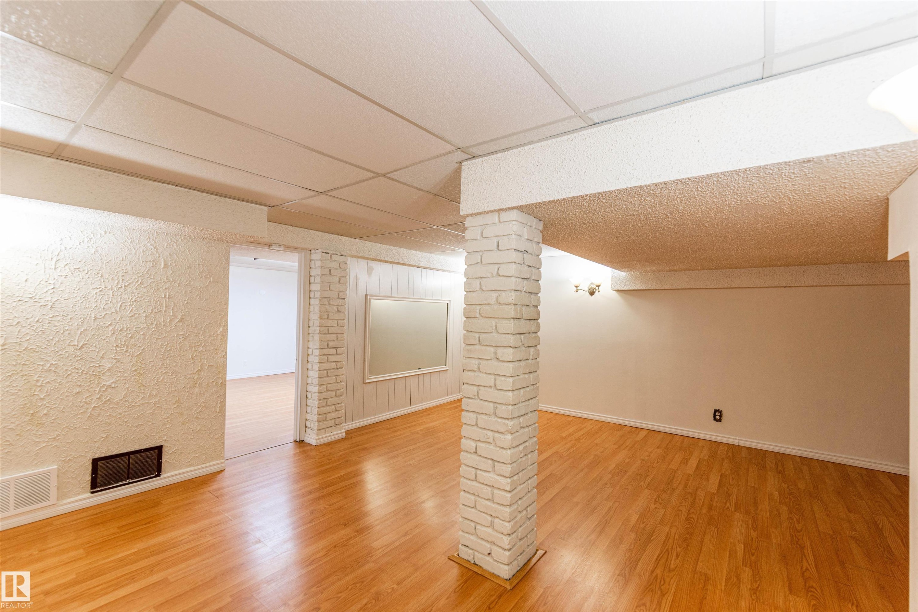 Spacious room featuring wood-finish flooring, a drop ceiling, and a painted brick column - 16524 116 Street, Edmonton, AB