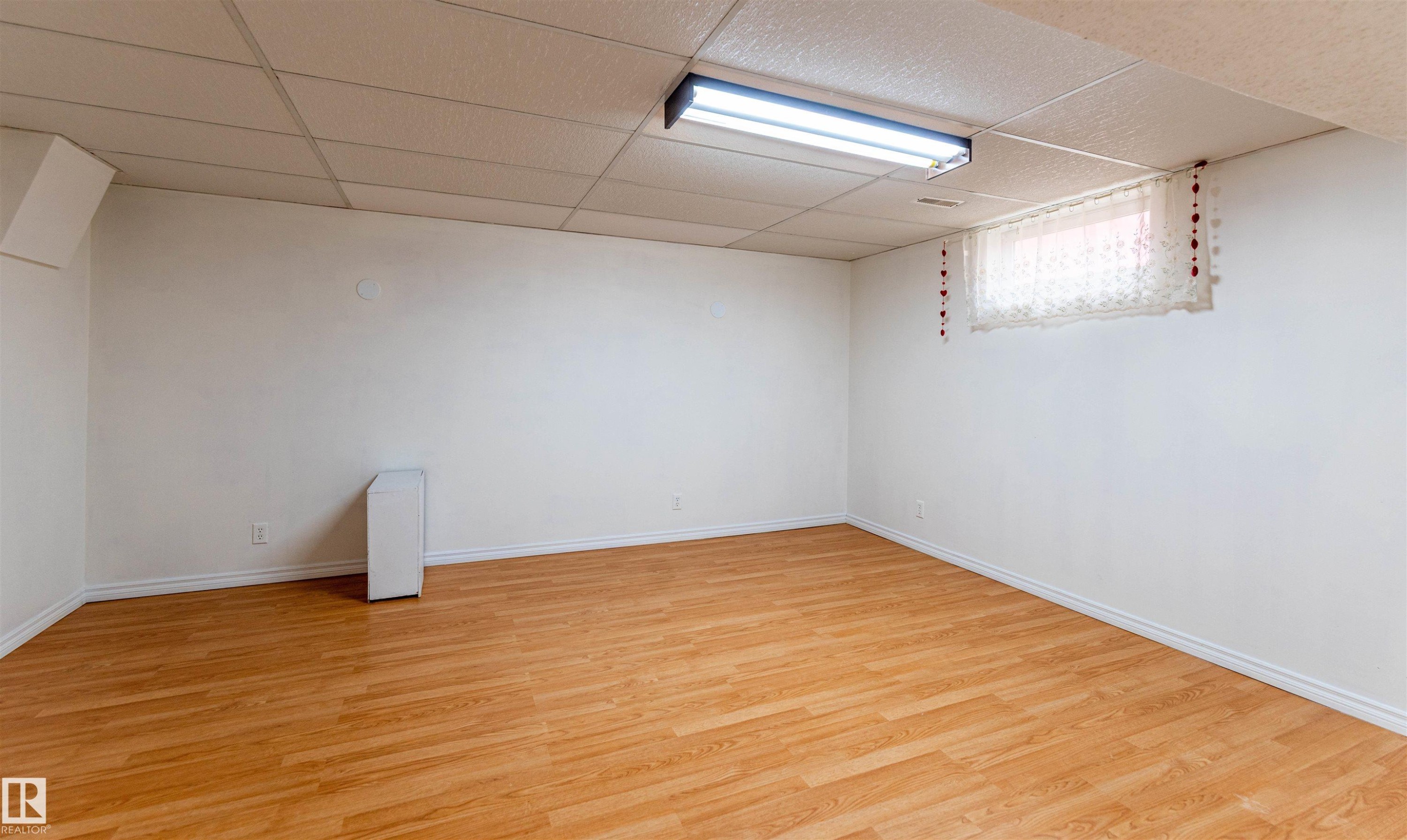 Spacious room featuring wood-finish flooring, white baseboards, and a drop ceiling with integrated fluorescent lighting - 16524 116 Street, Edmonton, AB