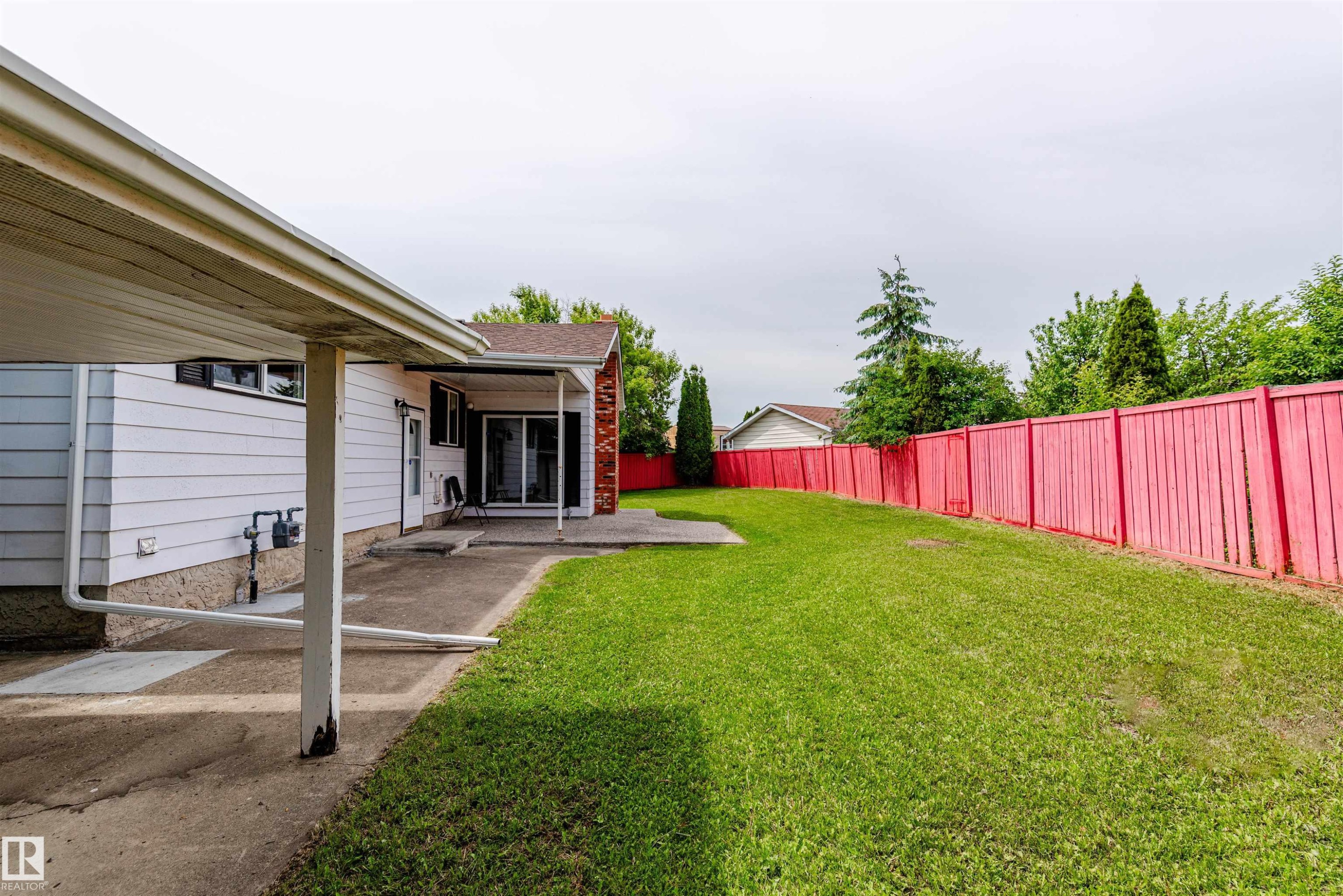 Expansive grassy backyard featuring a vibrant privacy fence, concrete patio, and a covered carport with direct access to the home - 16524 116 Street, Edmonton, AB