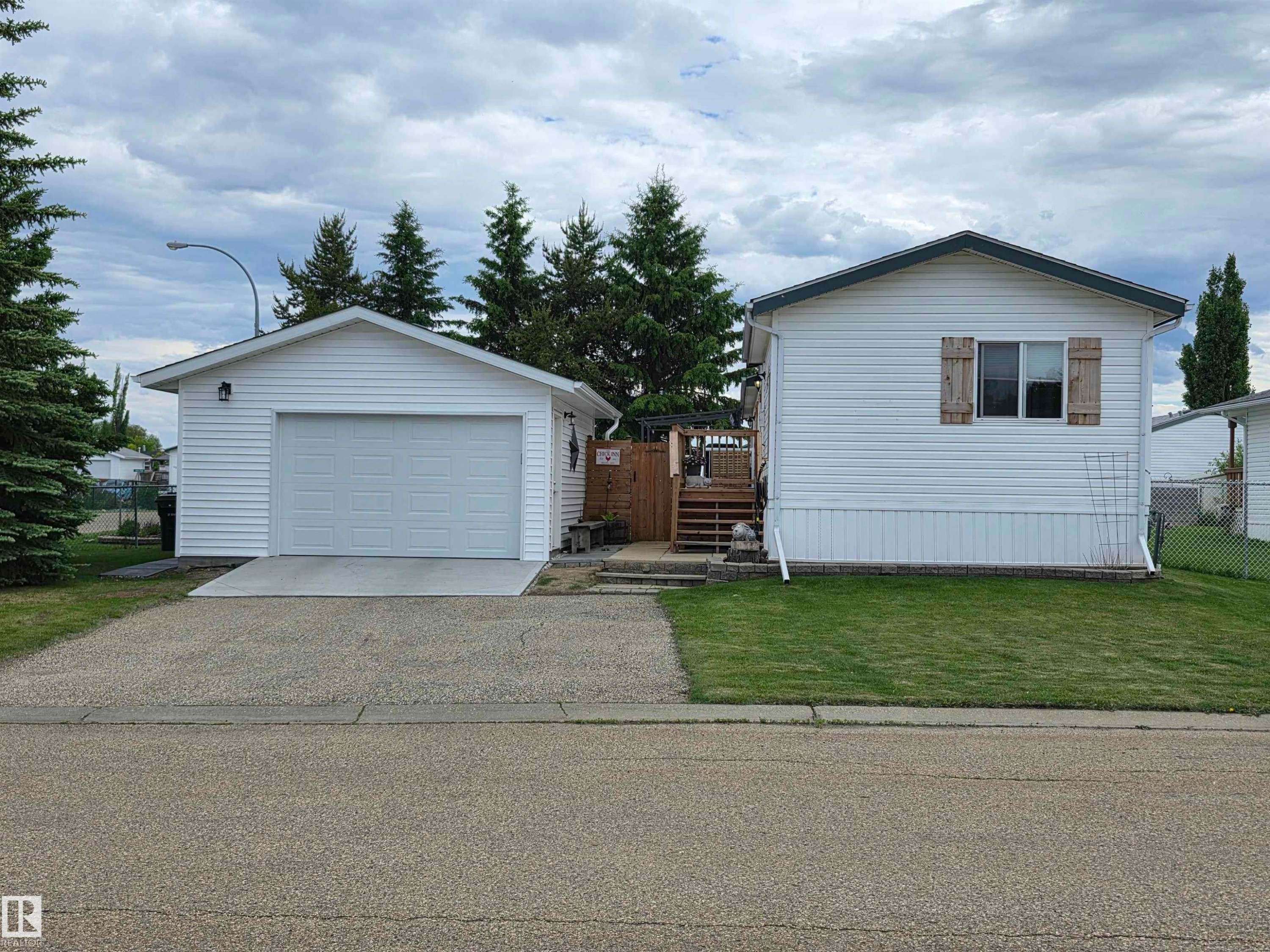 White siding residence featuring a detached single-car garage, a concrete driveway approach, and a front lawn with mature evergreen trees - 88B 3400 48 Street, Stony Plain, AB