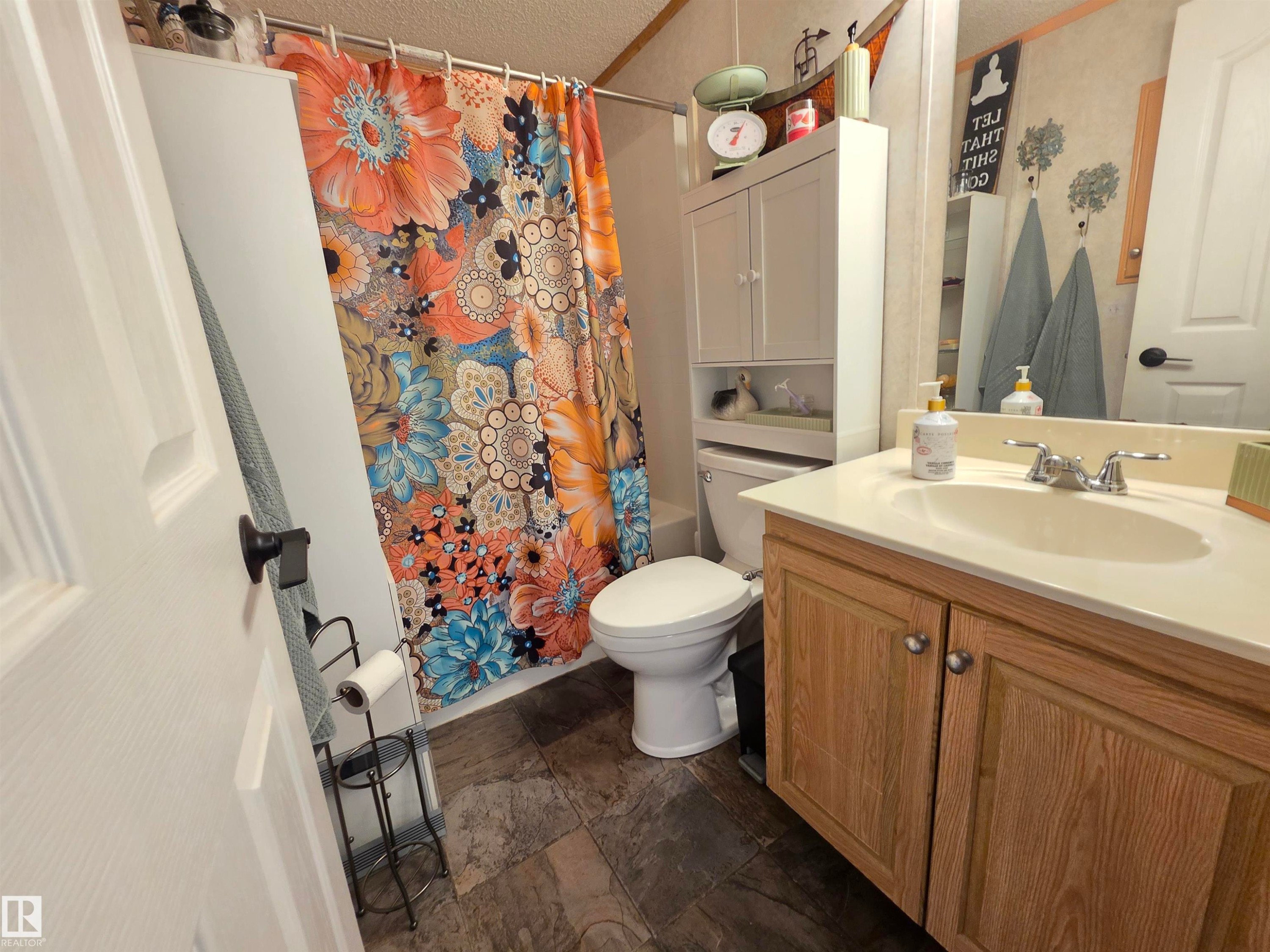 Bathroom featuring a single vanity with wood-finish cabinetry and an integrated sink, a commode, and a shower/tub combination - 88B 3400 48 Street, Stony Plain, AB