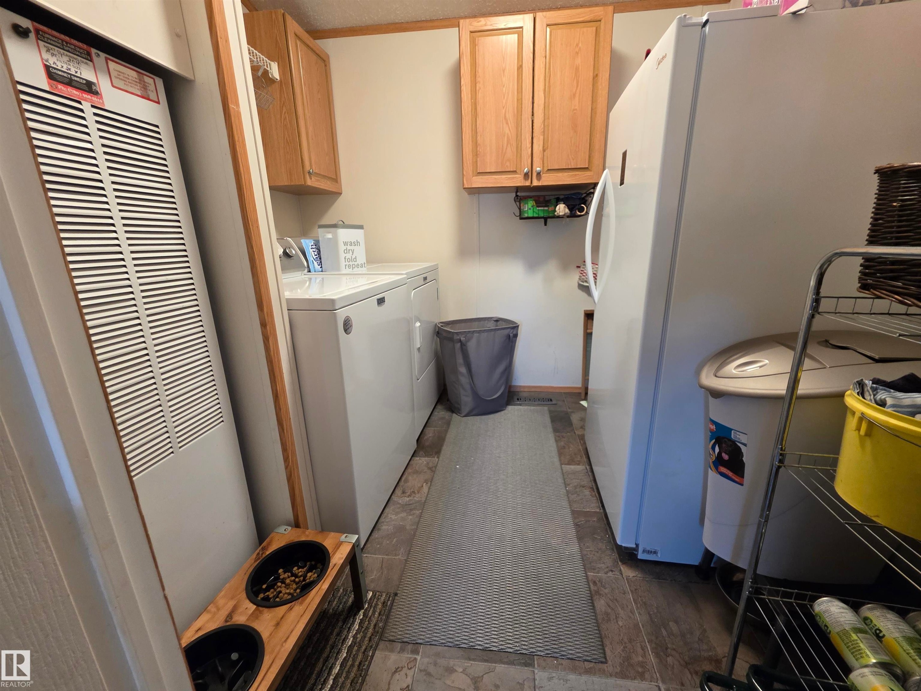 Dedicated laundry area featuring wood-finish flooring, two upper wood cabinetry units, a built-in furnace, and a visible washer and dryer - 88B 3400 48 Street, Stony Plain, AB
