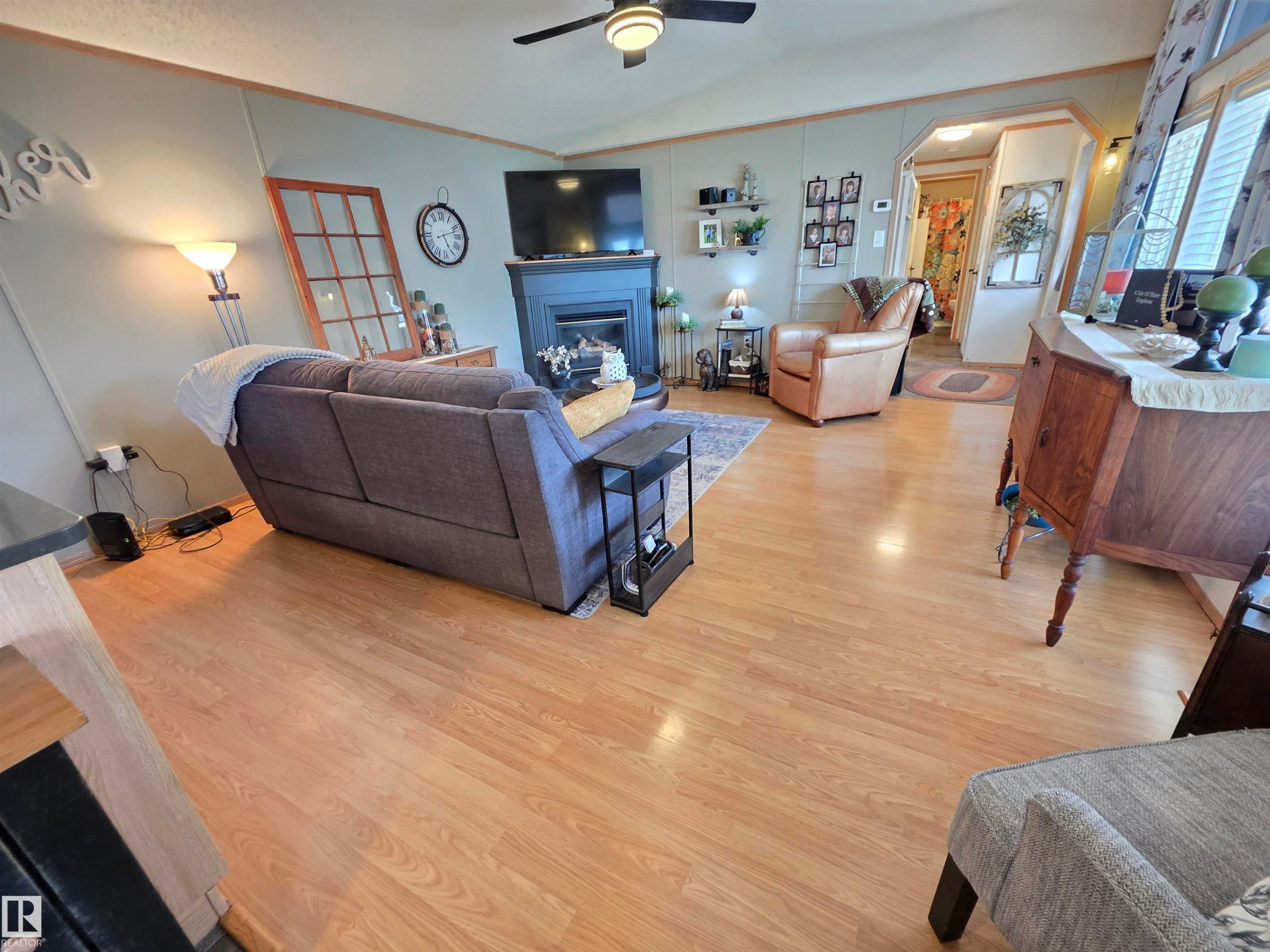 Living area featuring wood-finish flooring, a ceiling fan, and a fireplace with a dark mantel - 88B 3400 48 Street, Stony Plain, AB