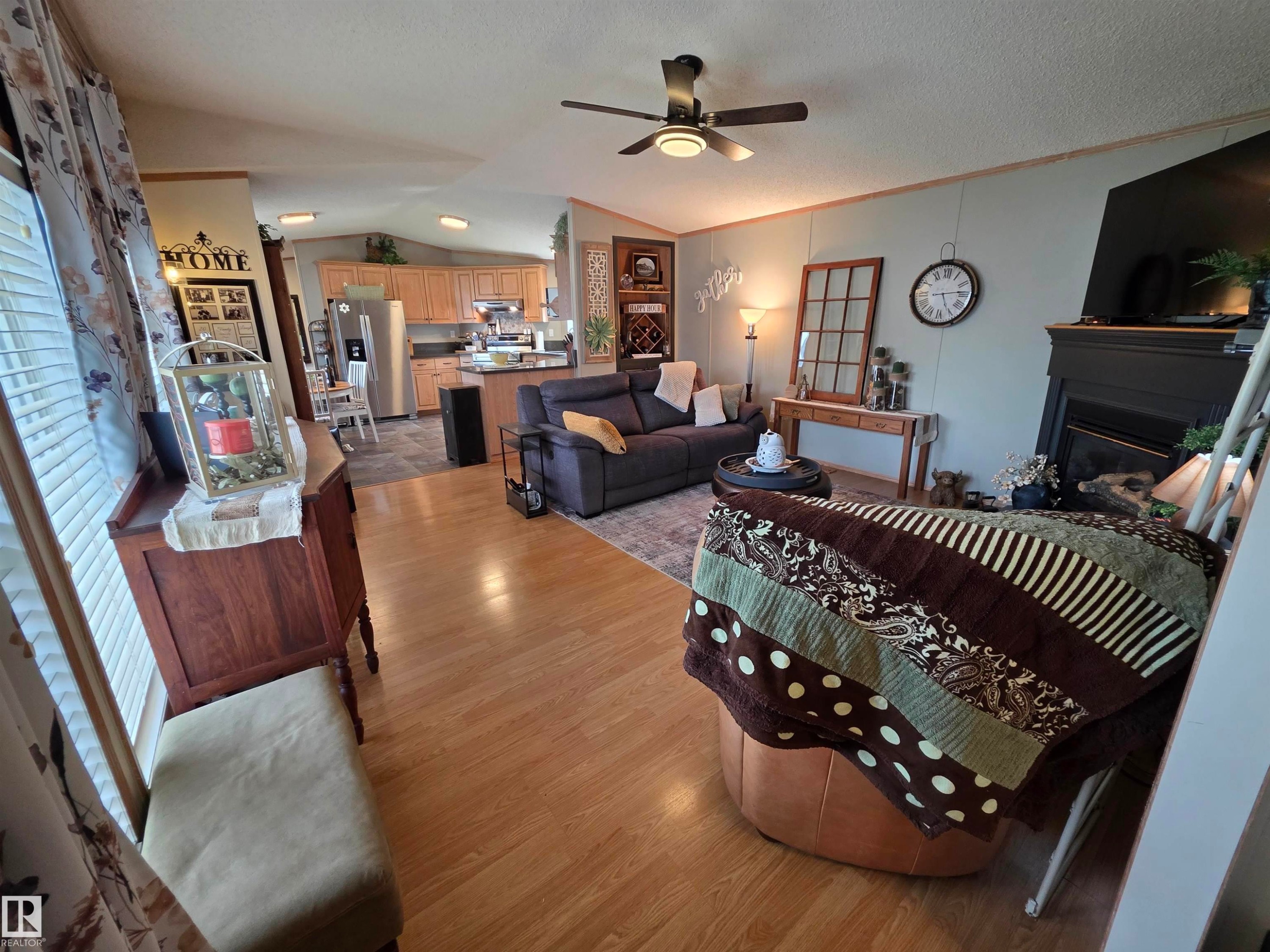 Open-concept living area with wood-finish flooring, a ceiling fan, and a fireplace with a black mantel - 88B 3400 48 Street, Stony Plain, AB