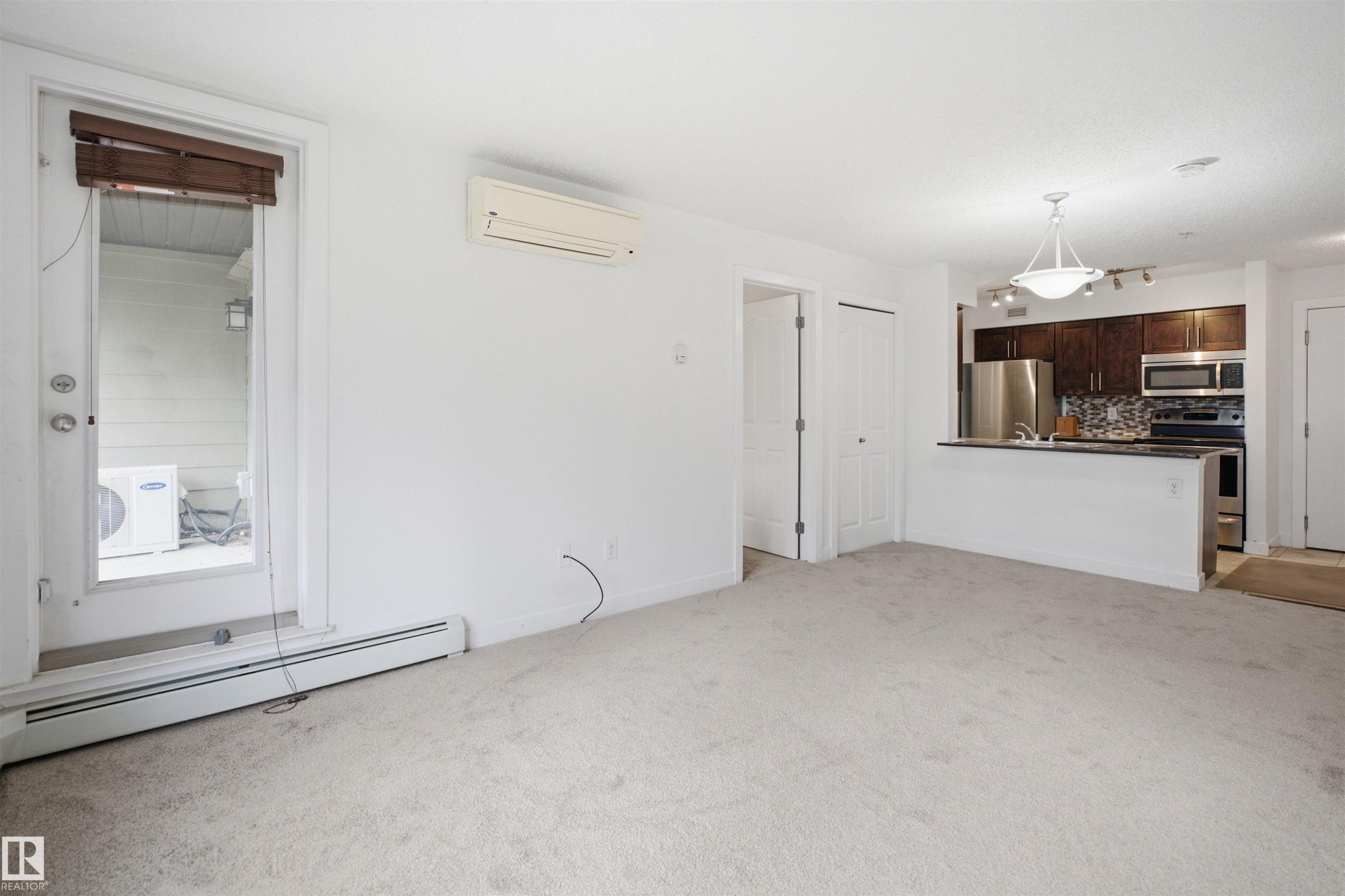 Open-concept living area featuring light-colored carpeting, a wall-mounted mini-split HVAC unit, and baseboard heating - 115 274 Mcconachie Drive, Edmonton, AB