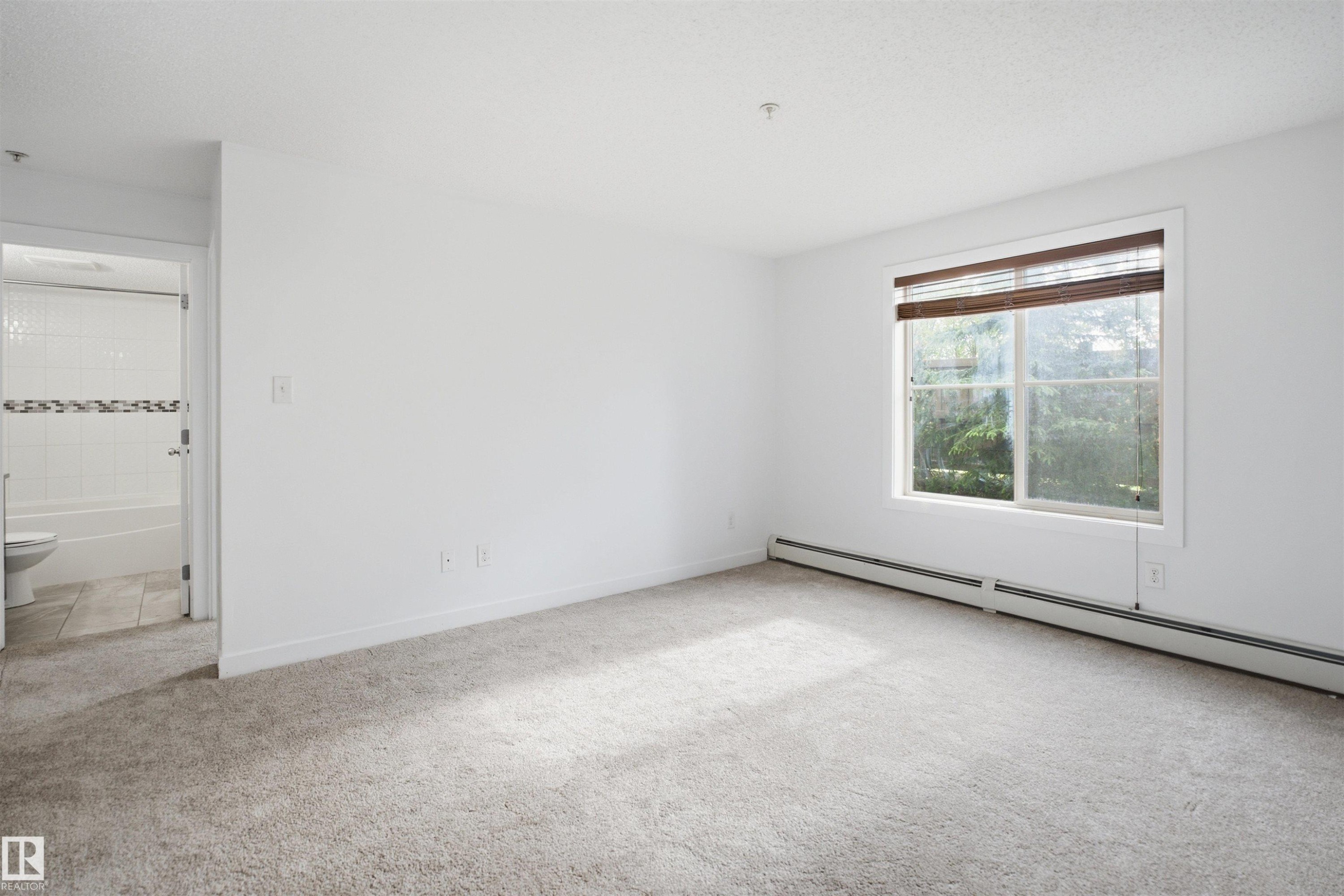 Carpeted room featuring a large window with natural light, window blinds, and baseboard heating - 115 274 Mcconachie Drive, Edmonton, AB