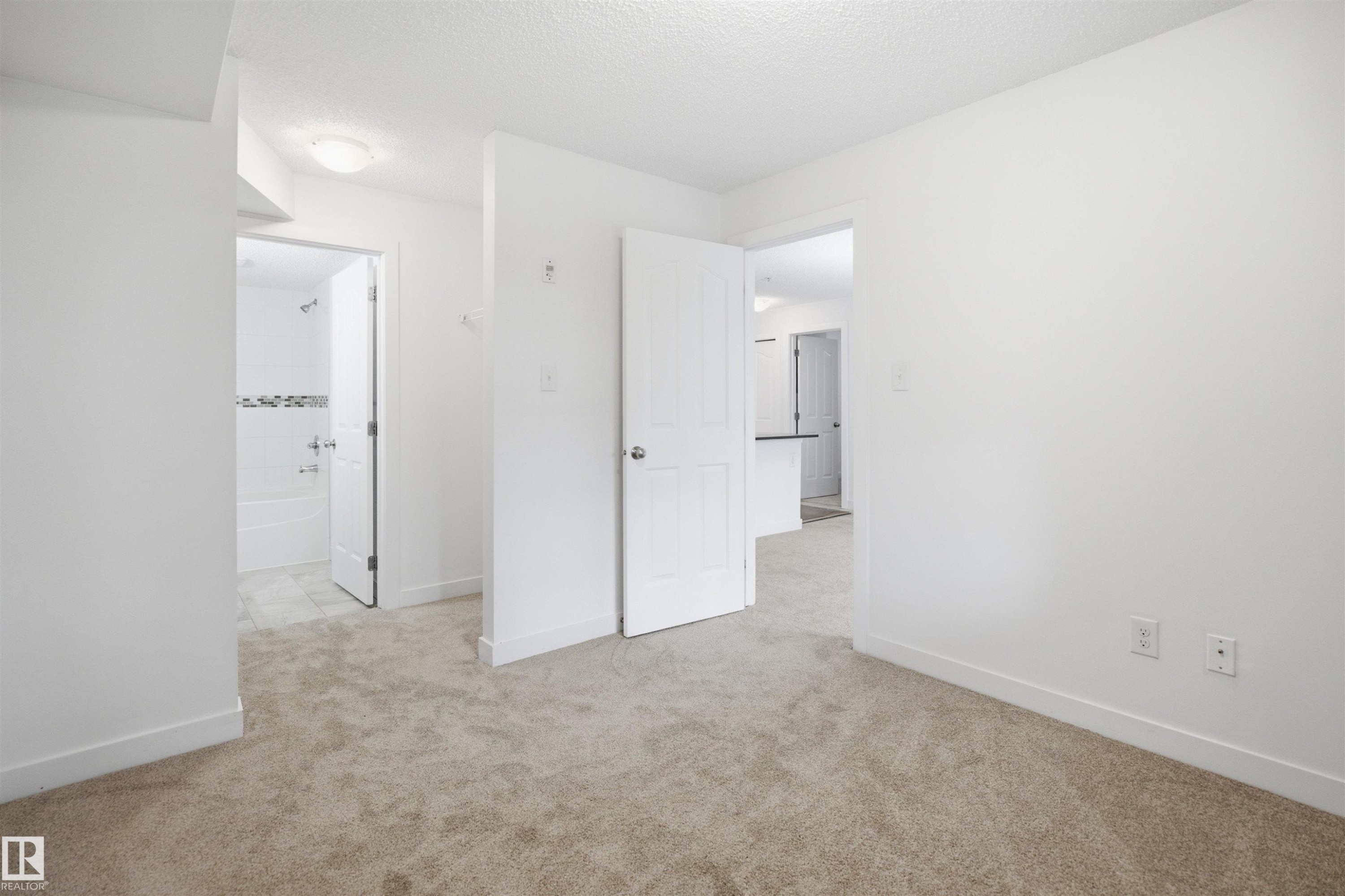Neutral-toned carpet flooring extends throughout the room, complemented by crisp white walls and baseboards - 115 274 Mcconachie Drive, Edmonton, AB